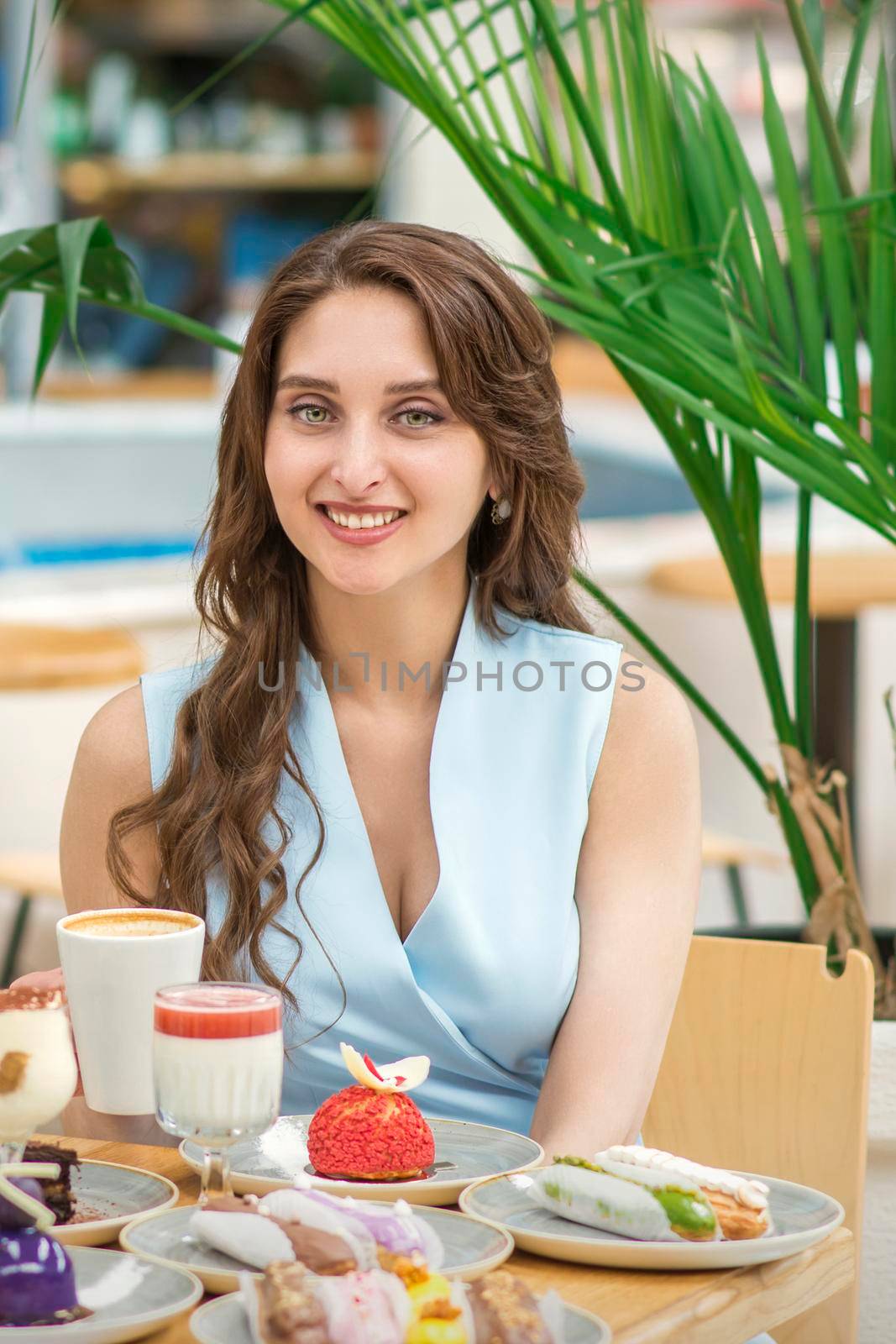 A beautiful young caucasian woman sitting at the table with cakes and a cup of coffee in cafe outdoor