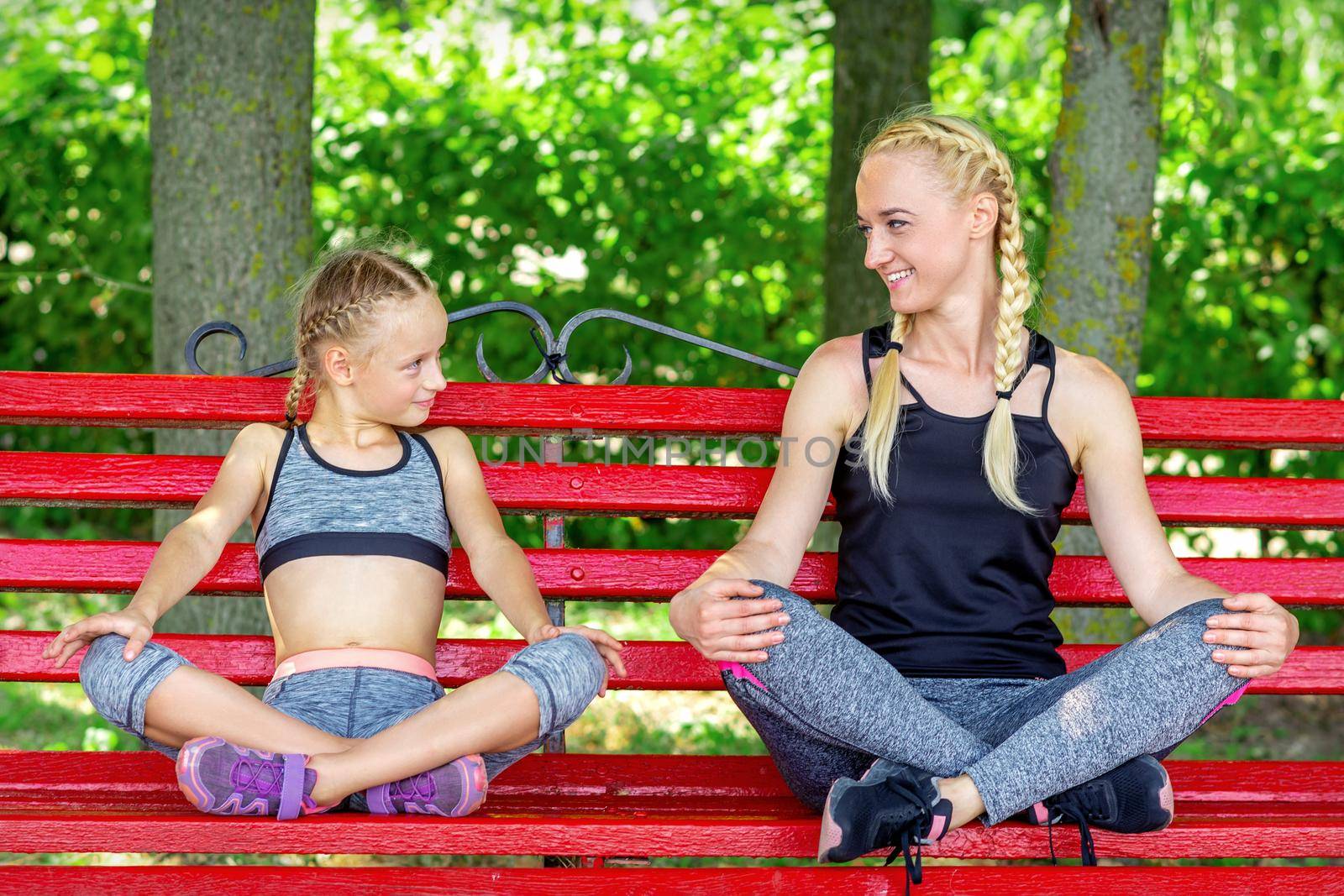 Mother with daughter wearing sportswear sitting on the bench in the summer park