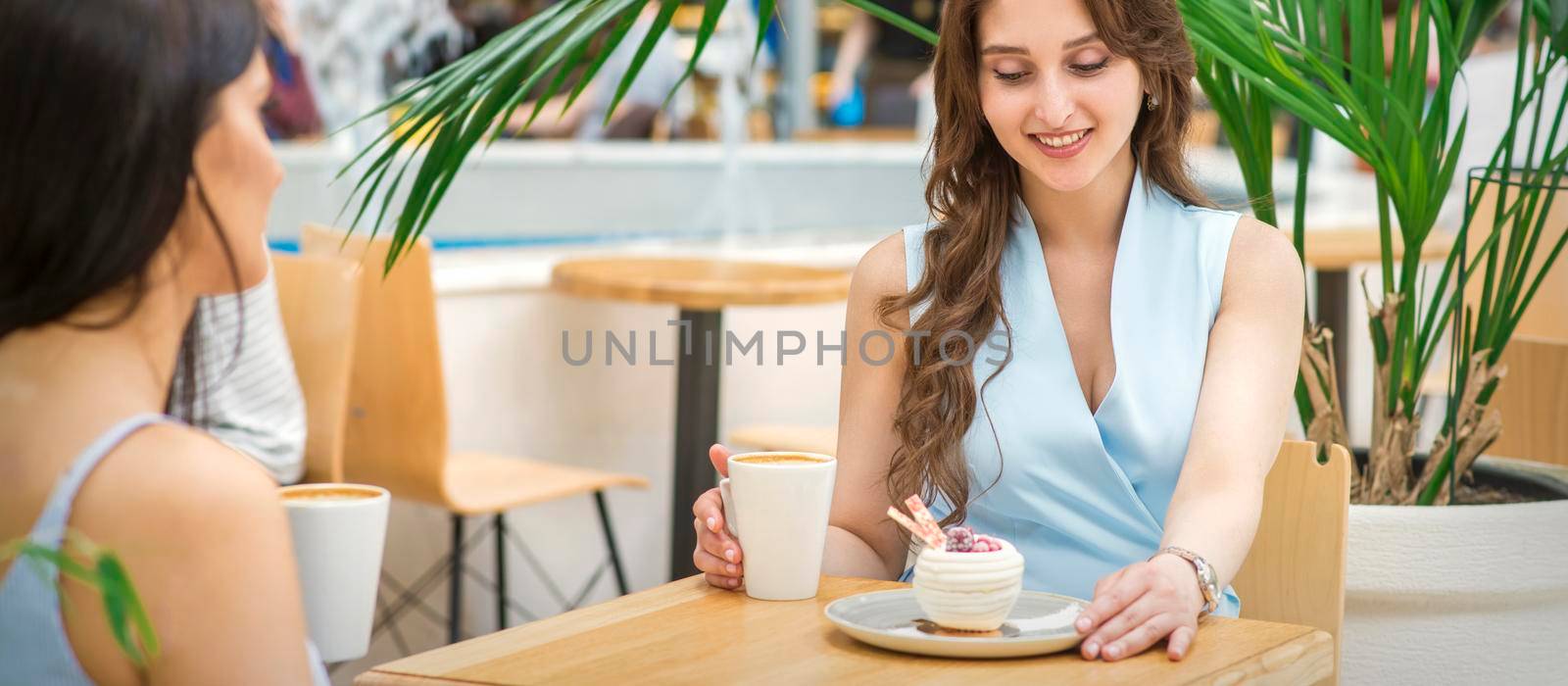 Two beautiful young caucasian women drink coffee sitting at the table in cafe outdoor
