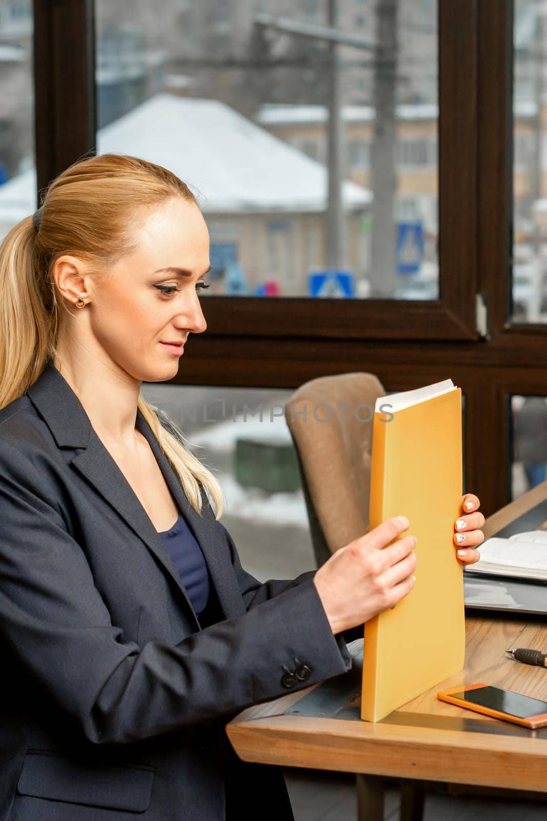 Beautiful young caucasian businesswoman holding a folder with documents sitting at the table in office or cafe
