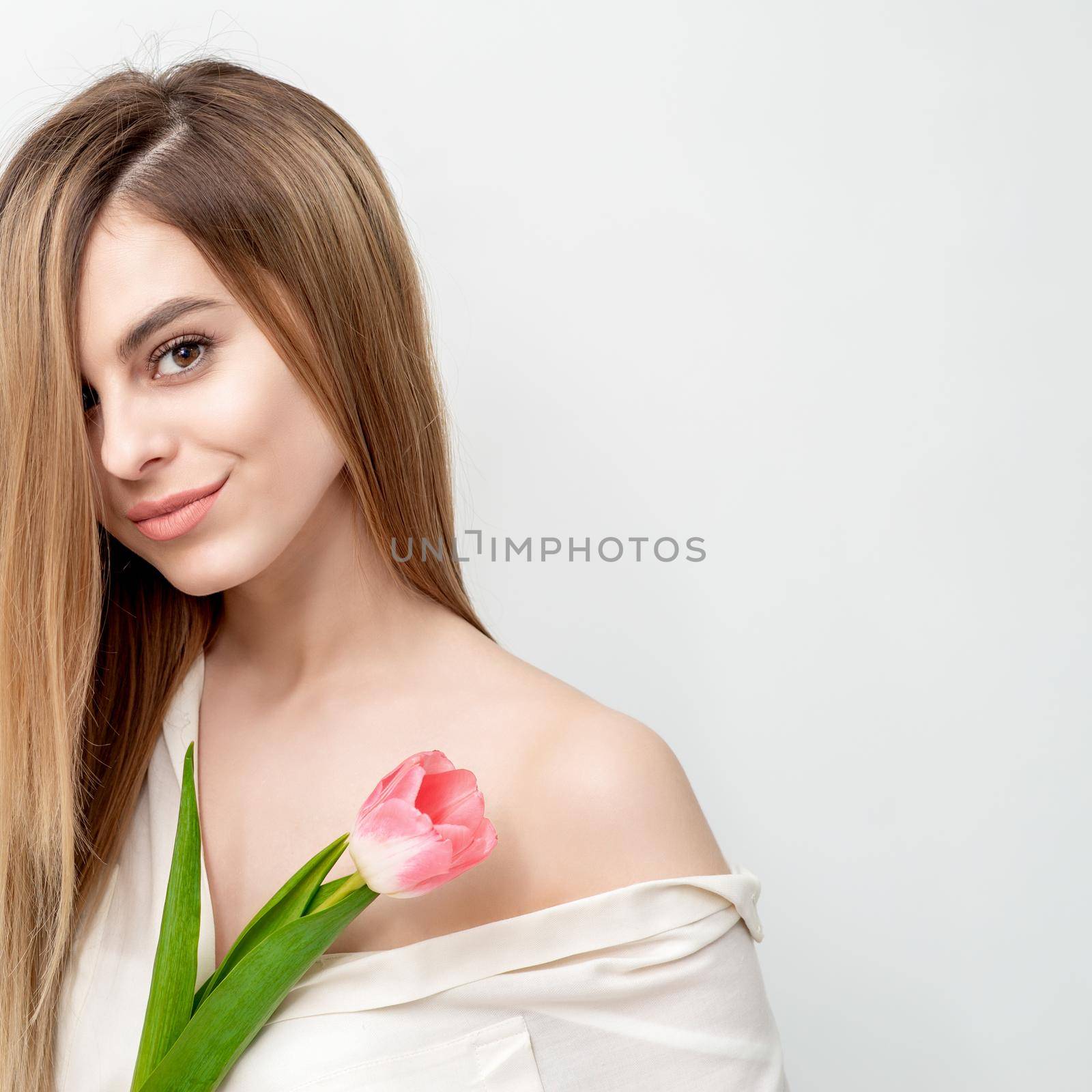 Portrait of a happy young caucasian woman with one pink tulip against a white background with copy space