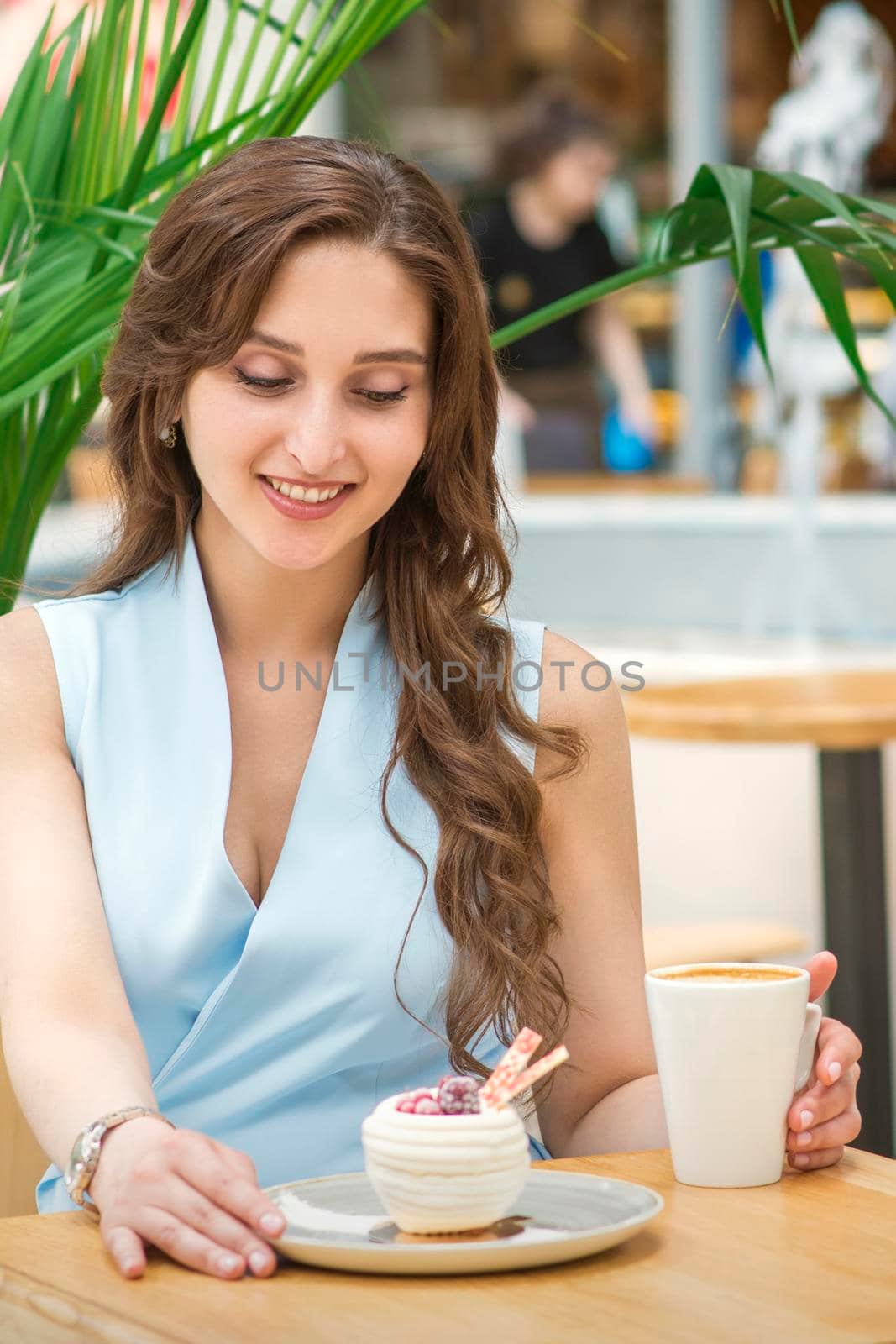 A beautiful young caucasian woman sitting at the table with cakes and a cup of coffee in cafe outdoor