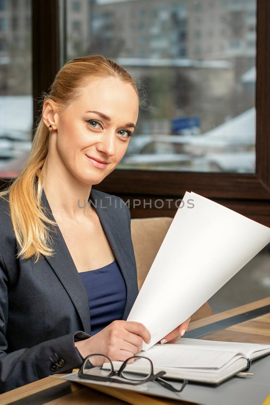 Portrait of a young smiling caucasian businesswoman prepares documents at the table looking at the camera in cafe