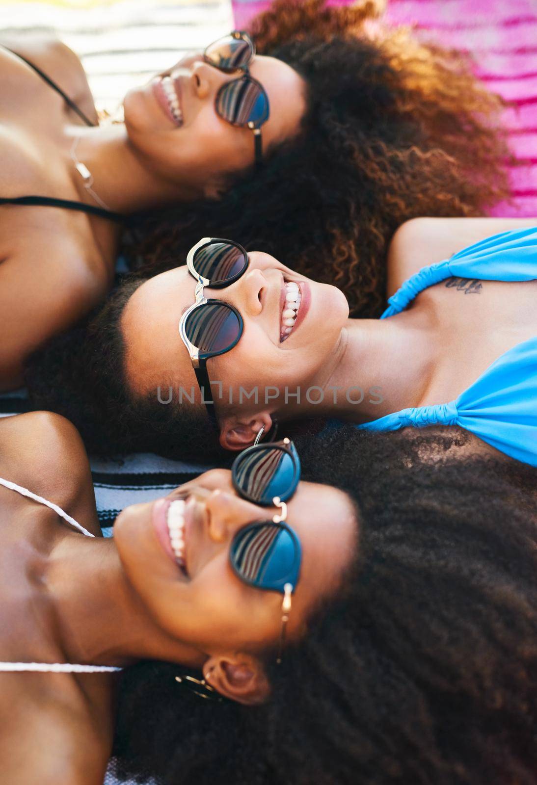 Beating the heat with the besties. a group of happy young women wearing sunglasses and relaxing at the beach. by YuriArcurs