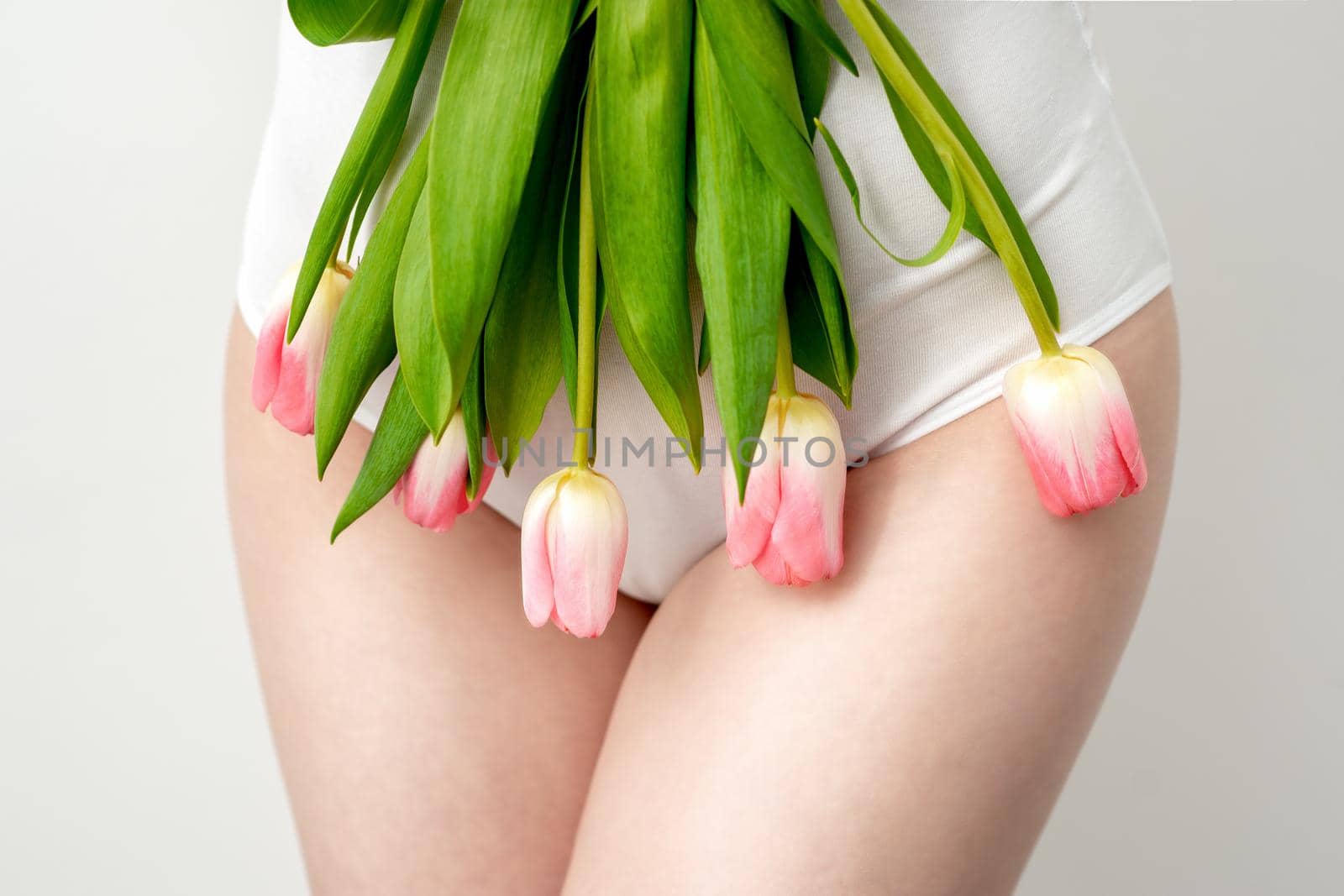 Bikini area of a young woman wearing a white underwear with pink tulips on white background