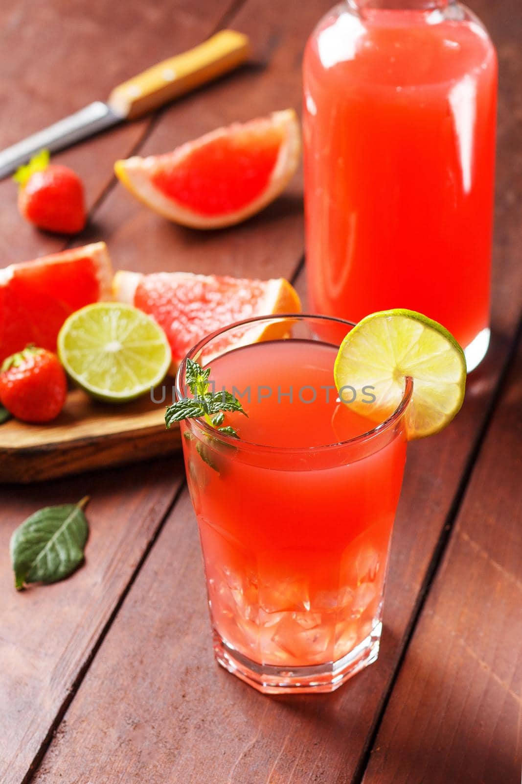 Fresh grapefruit juice in a glass with grapefruit pieces, lime and mint on a wooden background. vertical photo