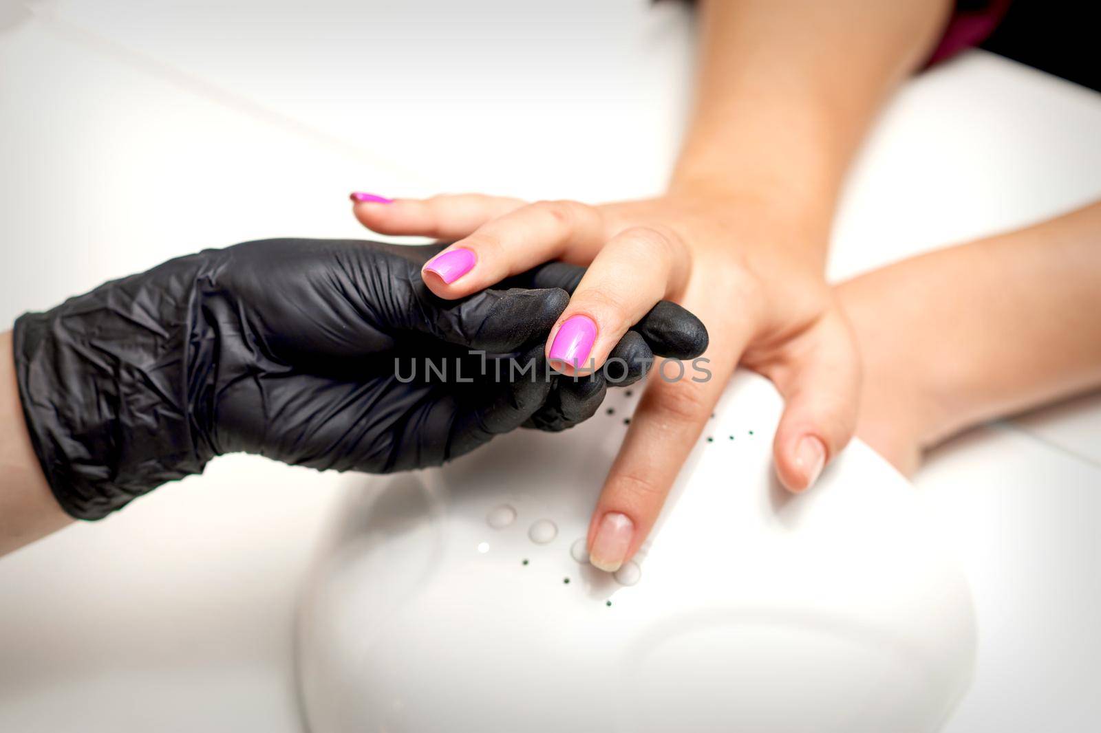 Manicure master's hand holds a female finger with purple nail polish while painting the nails in a nail salon