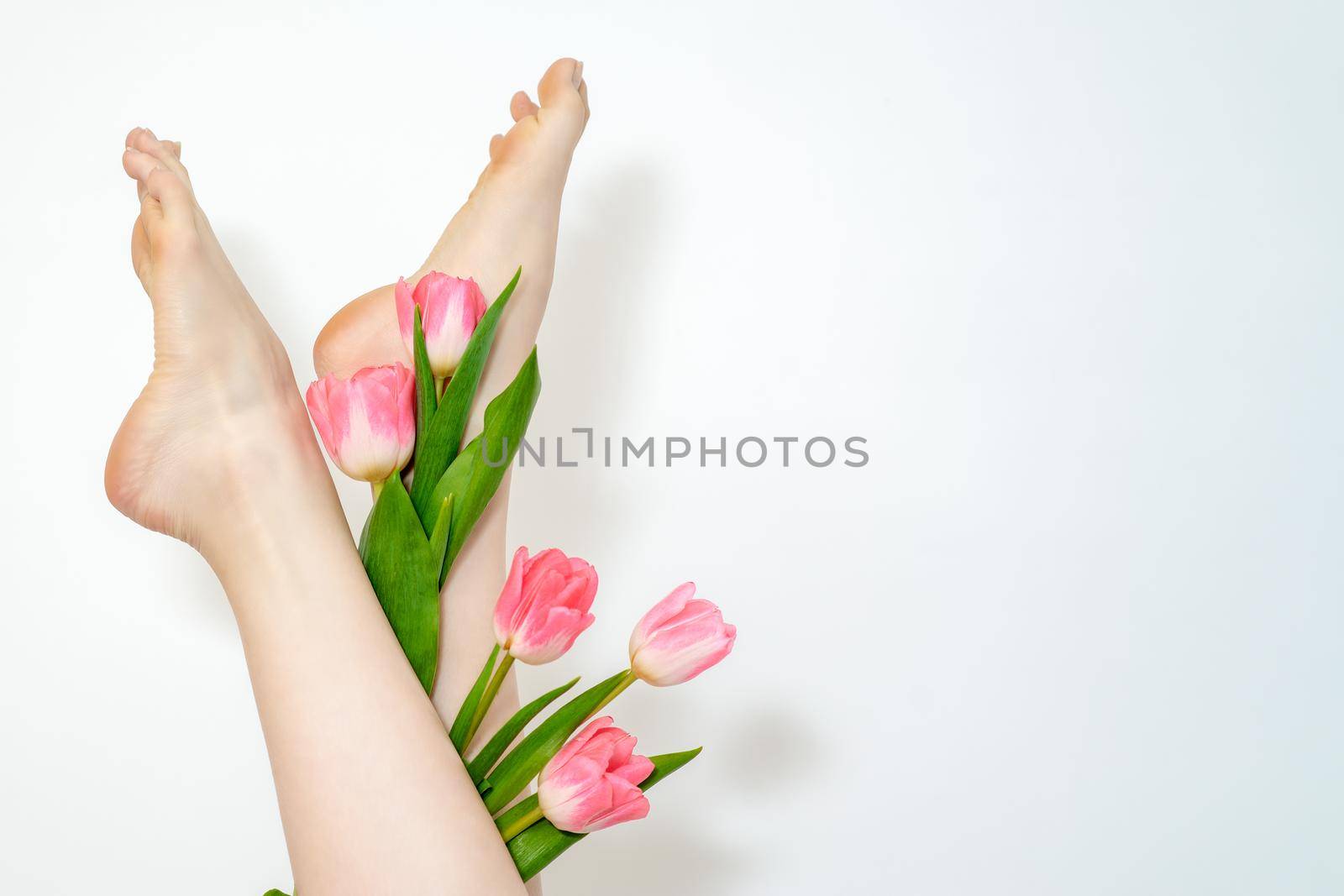 Beautiful slim smooth woman's legs with tulips flowers on white background