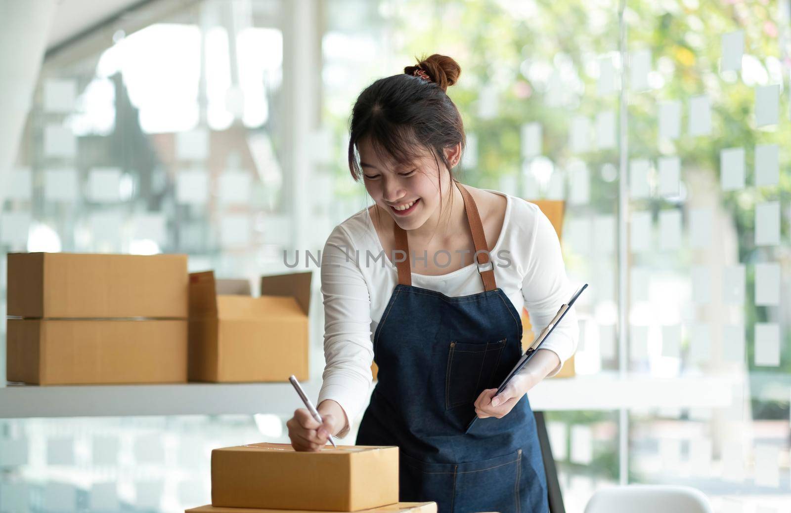 Startup happy Asian woman business owner works with a box at home, prepare parcel delivery SME supply chain, procurement, package box to deliver to customers, Online SME business entrepreneurs ideas, by wichayada