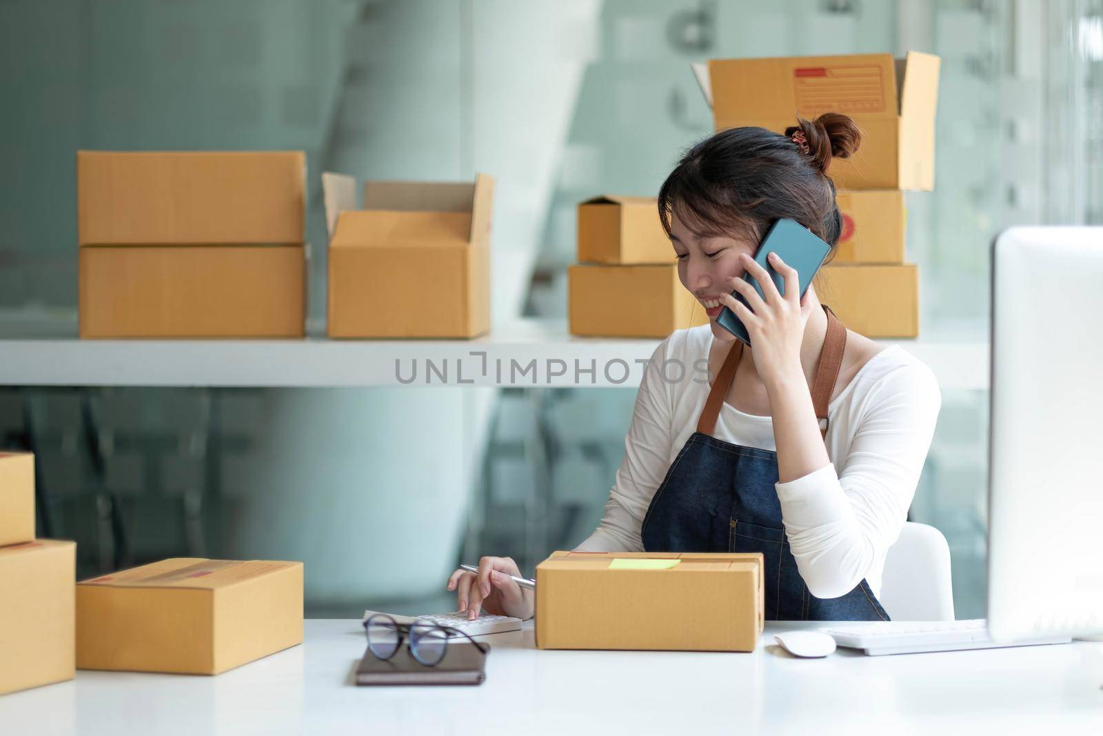 Closeup Asian smile Woman are receiving orders via cell phone and holding hand near laptop. Small business entrepreneur SME working with box at home, SME e-commerce digital technology concept. by wichayada