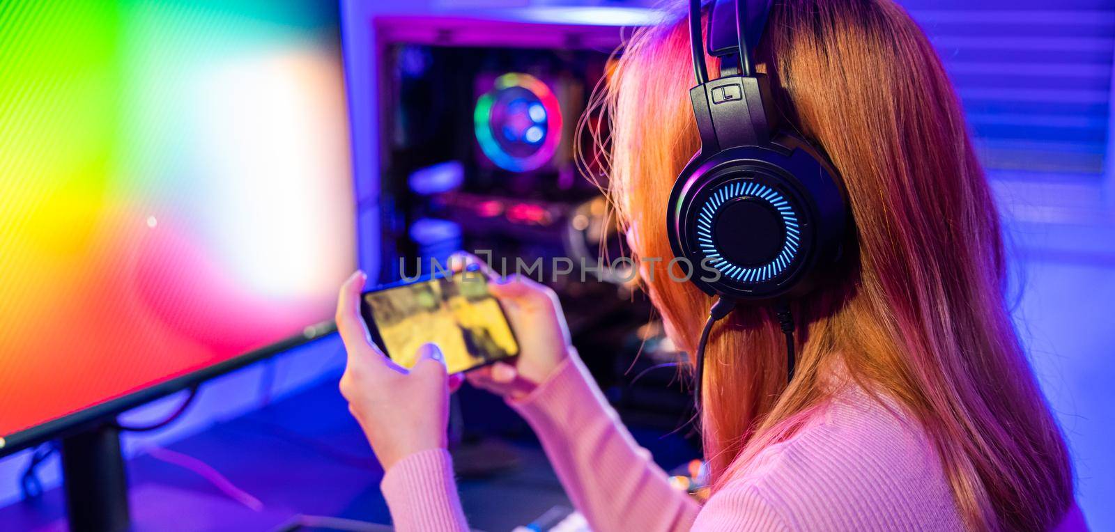 Asian woman live stream she play video game via smartphone at home neon lights living room, Gamer playing online game application on mobile phone wear gaming headphones, E-Sport concept