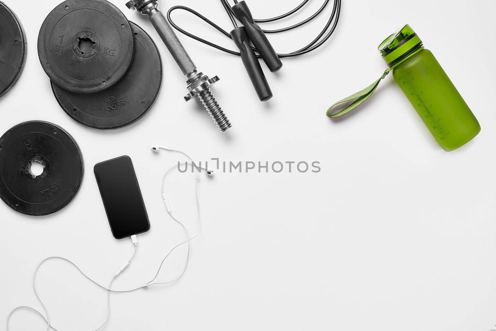 Fitness, healthy and active lifestyles concept, dumbbells, bottle of waters, smartphone with headphone, fitness bracelet on white background. Copy space for text. Top view. Flat lay. Still life