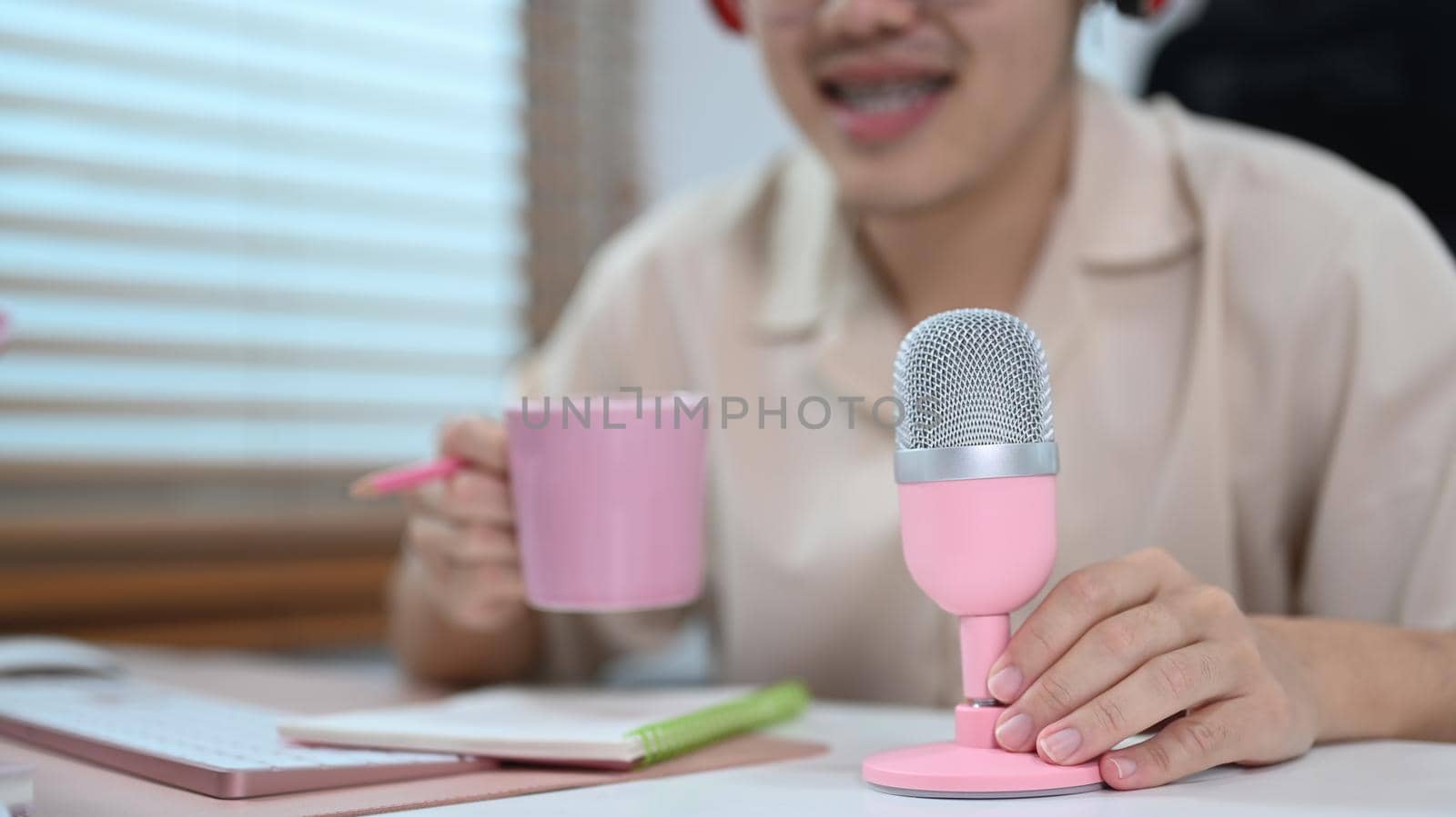 Cropped view of man sitting in front of microphone talking and recording podcast at home studio. Mass media, technology and people concept.