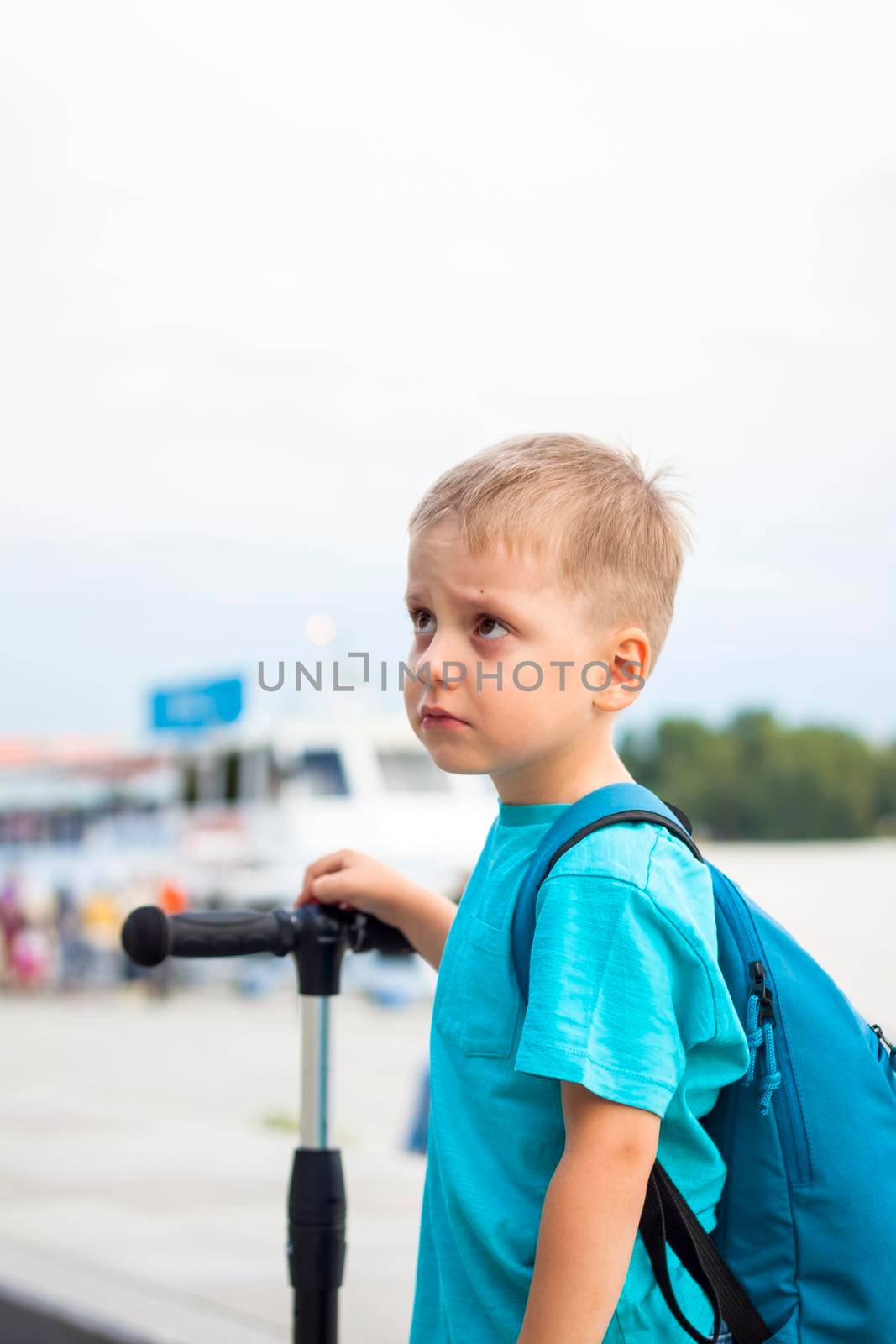 A boy on a scooter along the embankment of the city. Journey. Backpack on the back. The face expresses natural joyful emotions. Not staged photos from life.