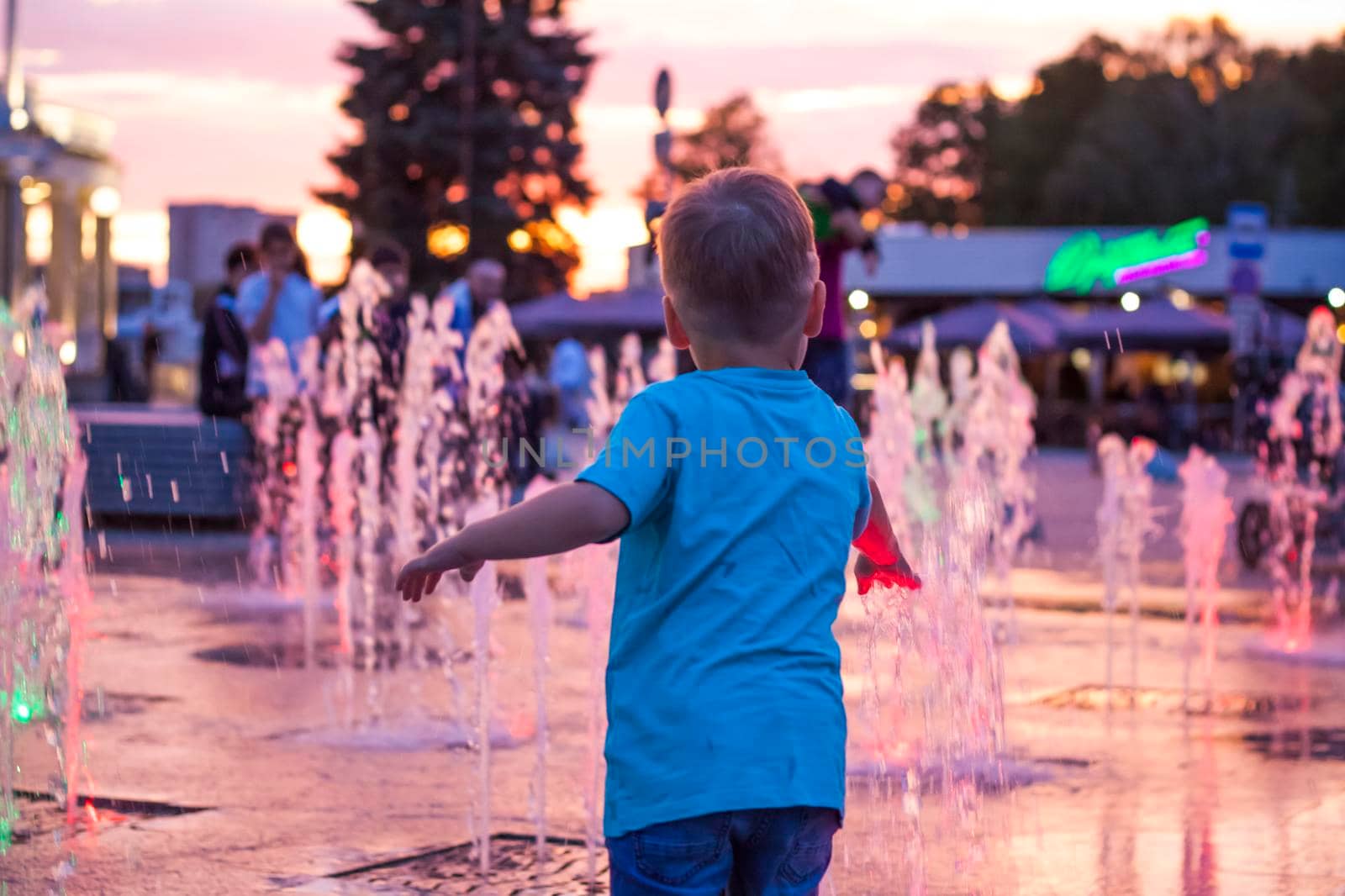 Children have fun frolicking in the fountains near the building in the park in the sunset light. Evening walk around the city