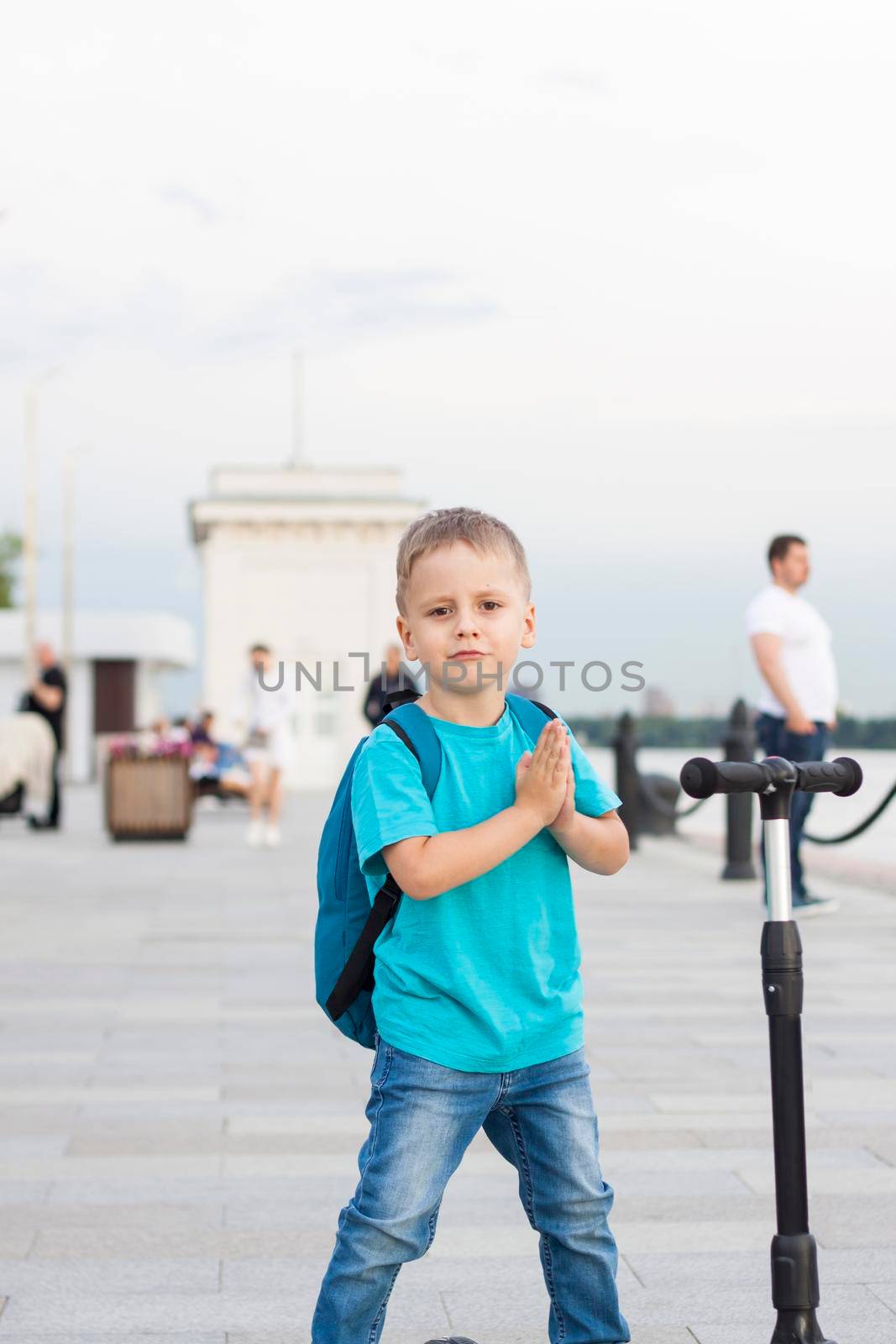 A boy on a scooter along the embankment of the city. Journey. Backpack on the back. The face expresses natural joyful emotions. Not staged photos from life.