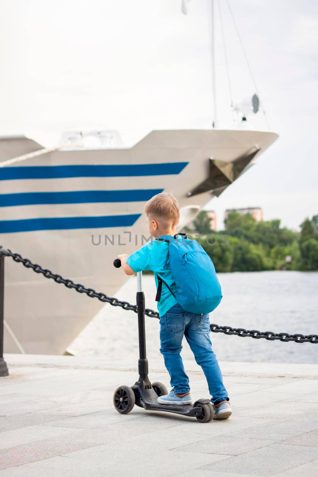 A boy on a scooter along the embankment of the city. Journey. Backpack on the back. The face expresses natural joyful emotions. Not staged photos from life.