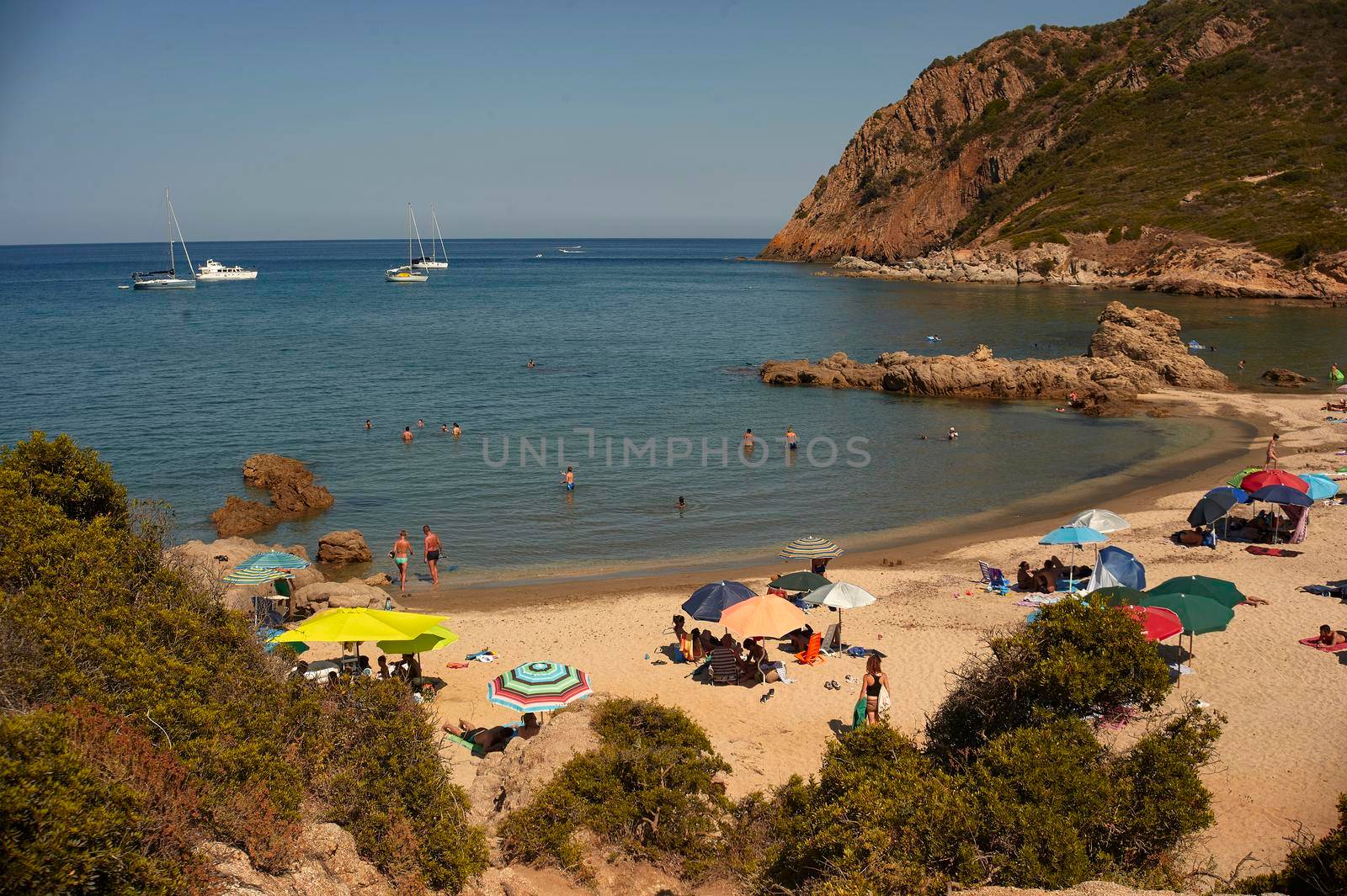 Beach of southern Sardinia (Cala Sa Figu) inserted in a natural bay full of tourists with umbrellas on vacation.