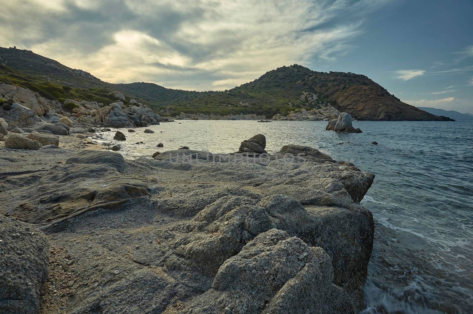 Beautiful Mediterranean beach typical of the coast of southern Sardinia taken over in summer. The beach, the rocks and the mountains behind blend in a wonderful panorama of amazing beauty.