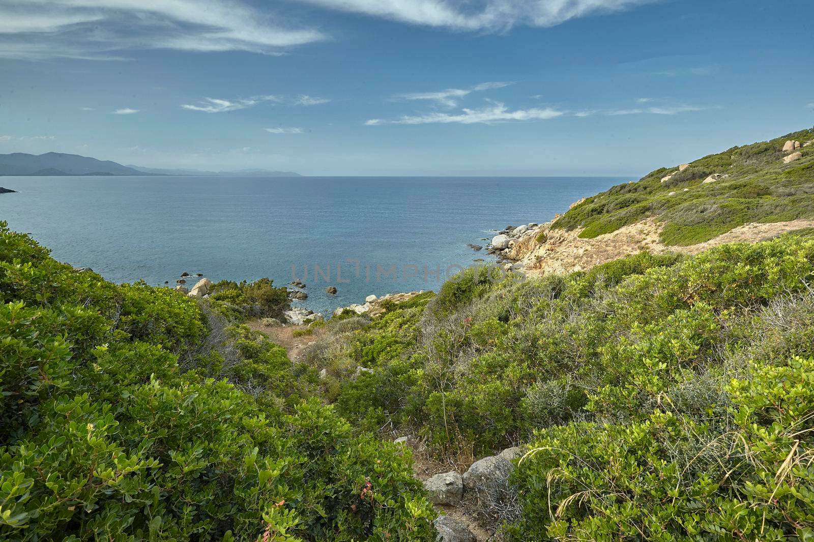 A glimpse of a southern coastline of Sardinia rich in green shrubs overlooking the blue and pristine sea.