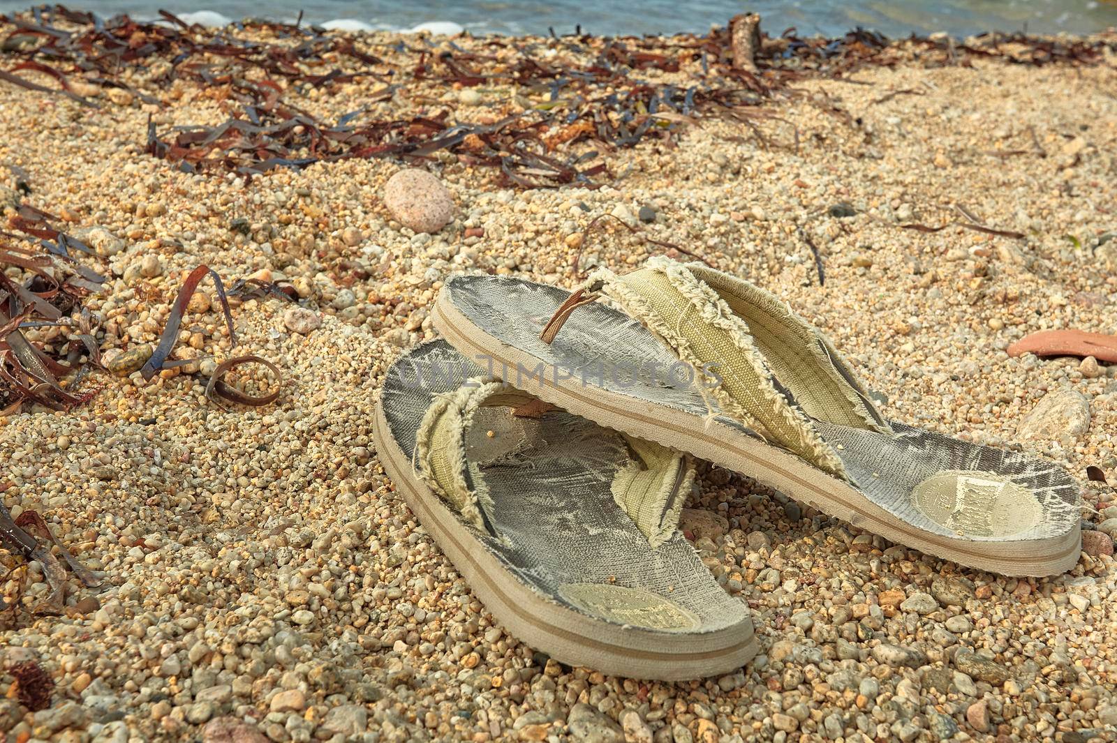 Pair of worn and worn flip-flops abandoned on the sand of the Mediterranean beach.