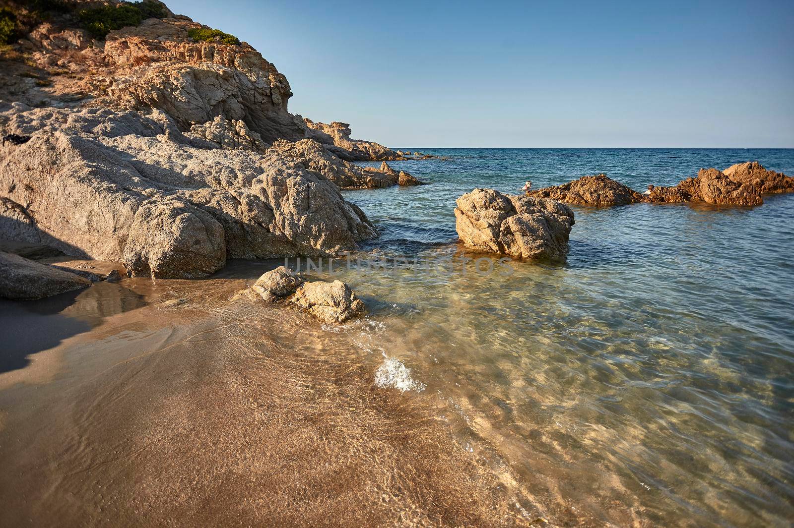 The place where the great rocks of the Sardinian coast meet the crystalline sea during a summer sunset.