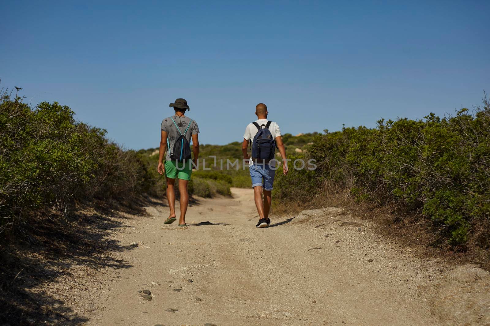 Couple of hikers walk along a dirt mountain path in the south of Sardinia.