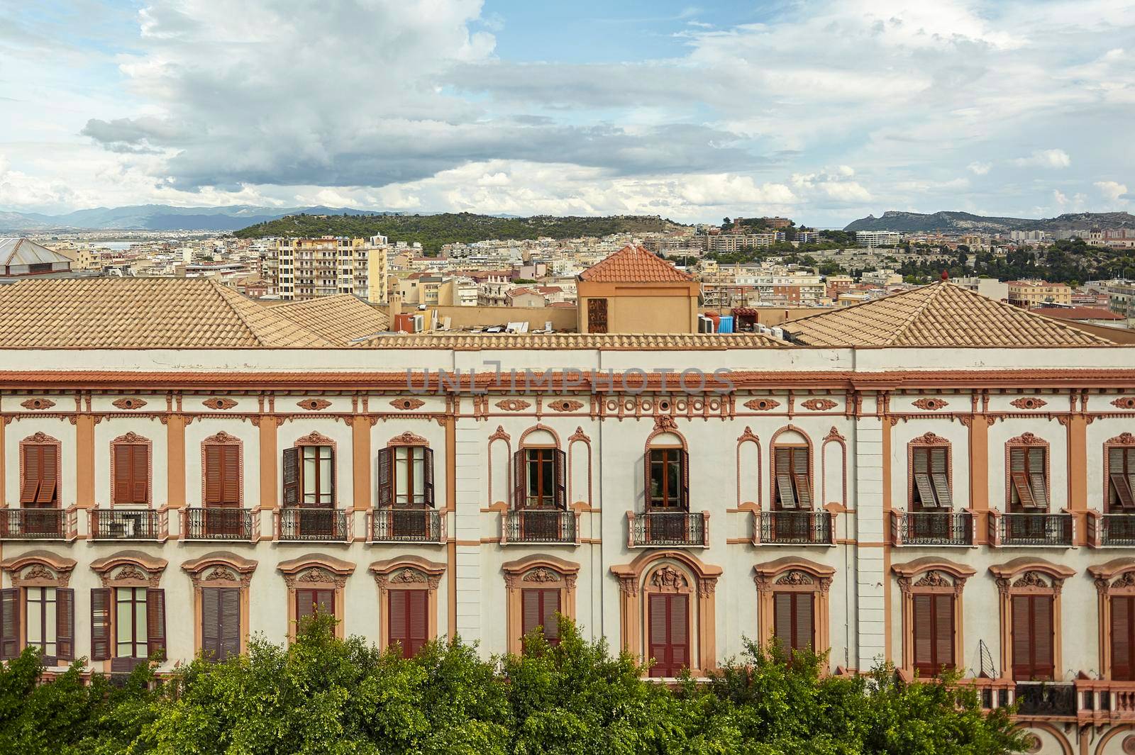 Side detail of a historic building in the city center of Cagliari in Italy, with behind the city panorama under a sky full of clouds.