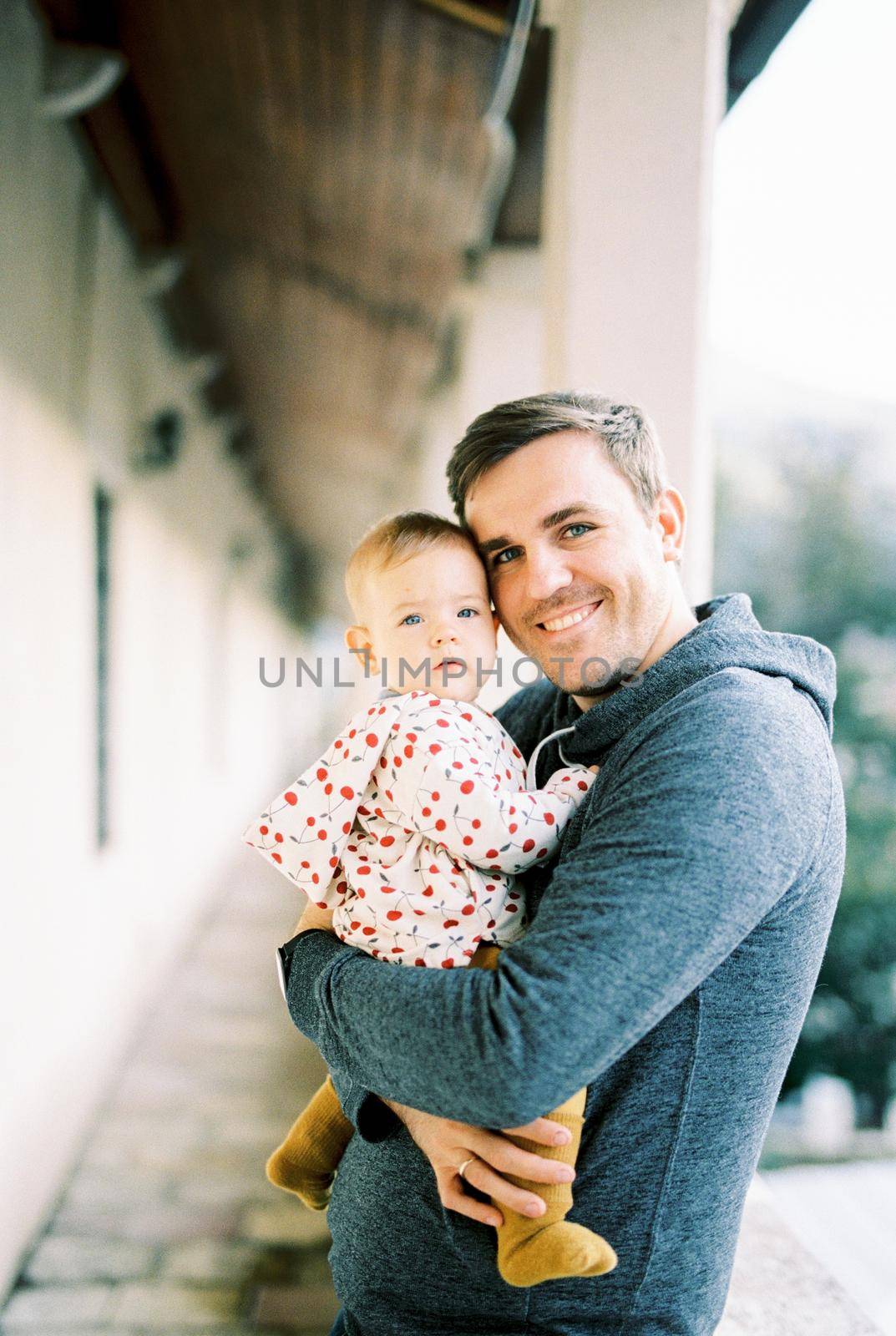 Smiling dad with a baby in his arms stands on the terrace. Portrait. High quality photo