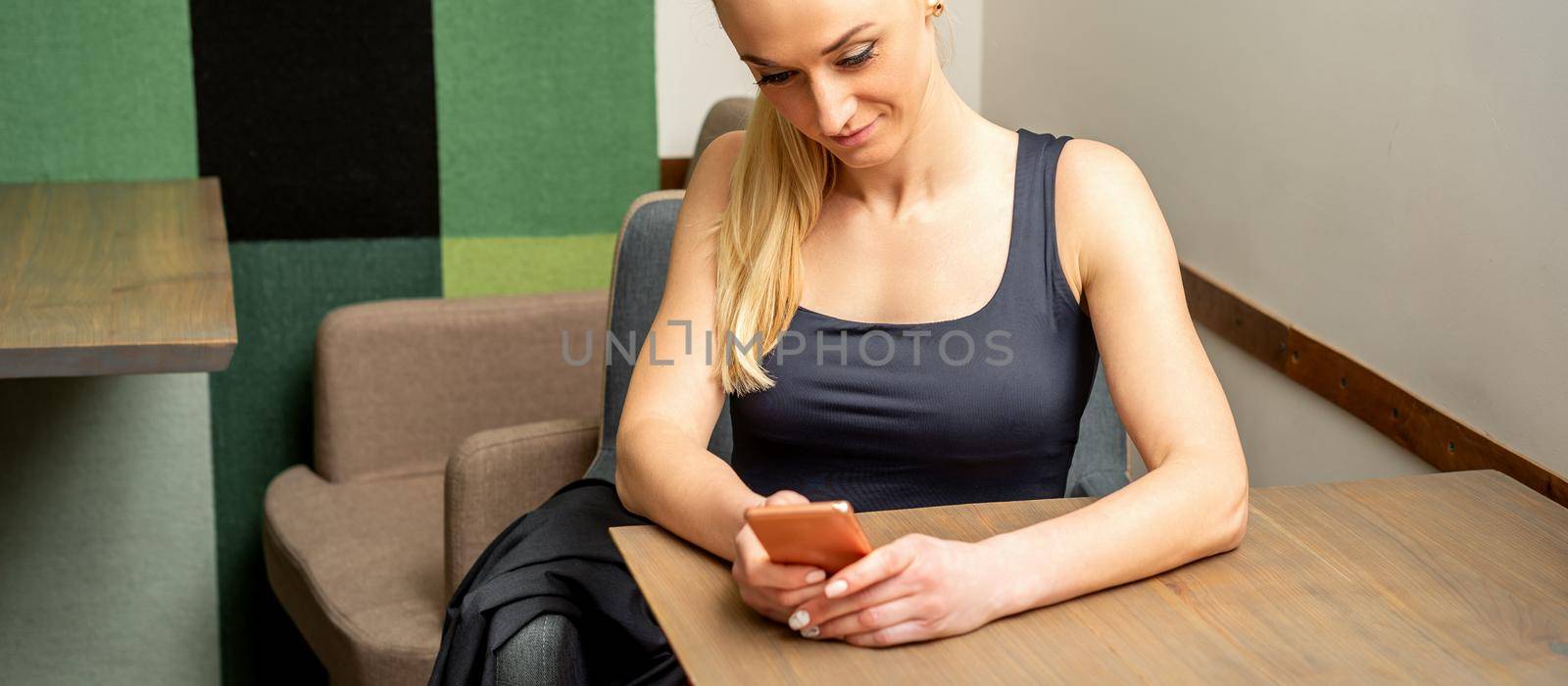 Beautiful young caucasian woman looking at smartphone sitting at the table in a cafe