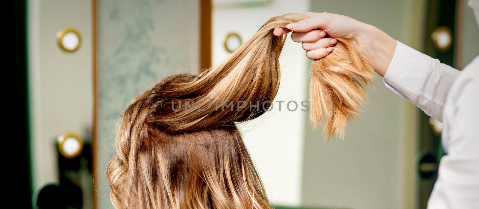 Hairdresser holds a strand of long hair of a young woman in a beauty salon