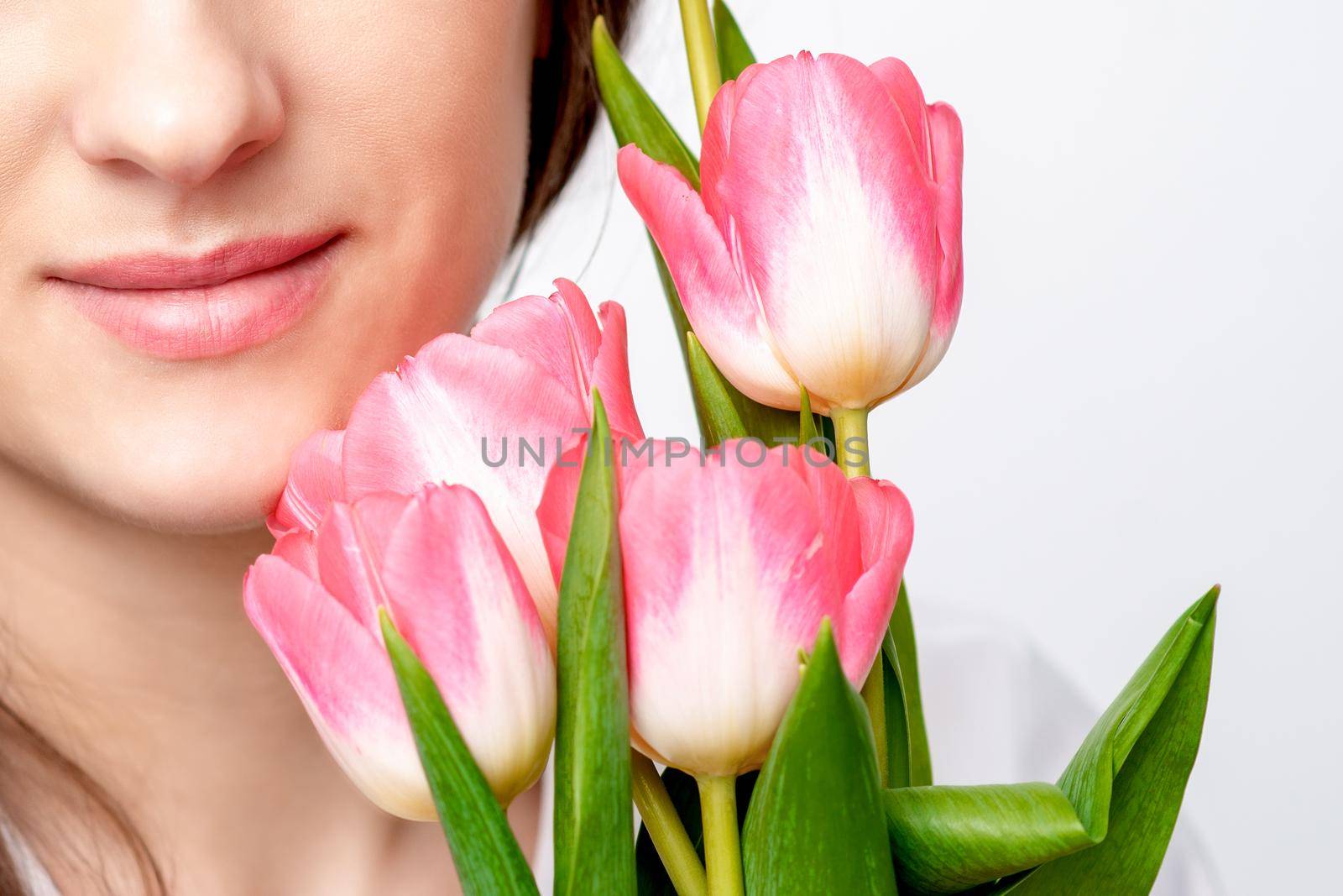 Half face portrait of a happy young caucasian woman with pink tulips against a white background