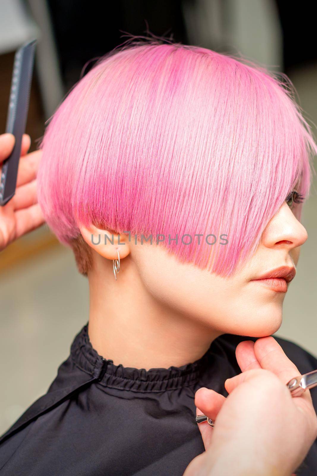 Male hairdresser makes short pink hairstyle for a young caucasian woman in a beauty salon