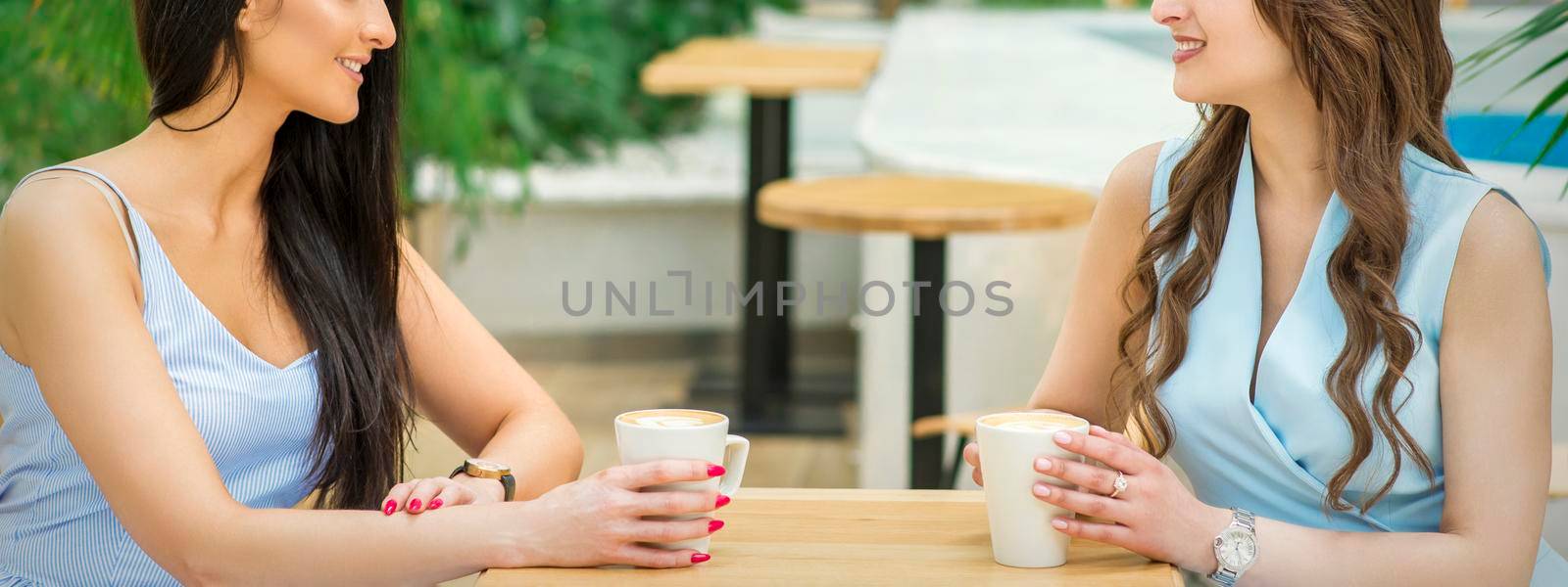 Two beautiful young caucasian women drink coffee sitting at the table in cafe outdoor