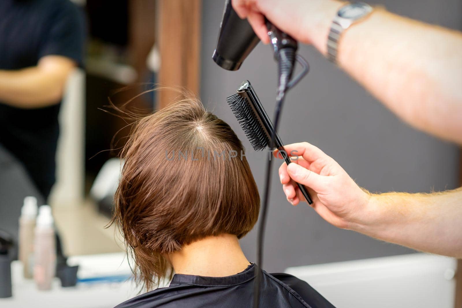 Hairdresser dries brown hair of the young woman in a beauty salon