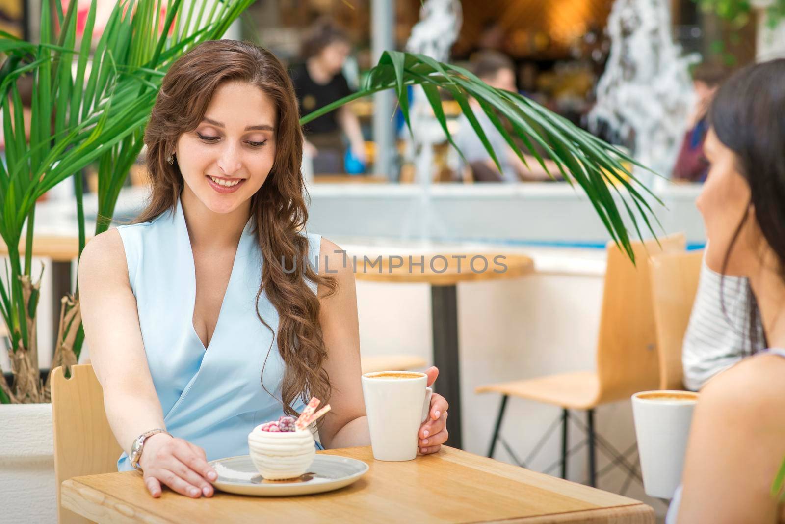 Two beautiful young caucasian women drink coffee sitting at the table in cafe outdoor