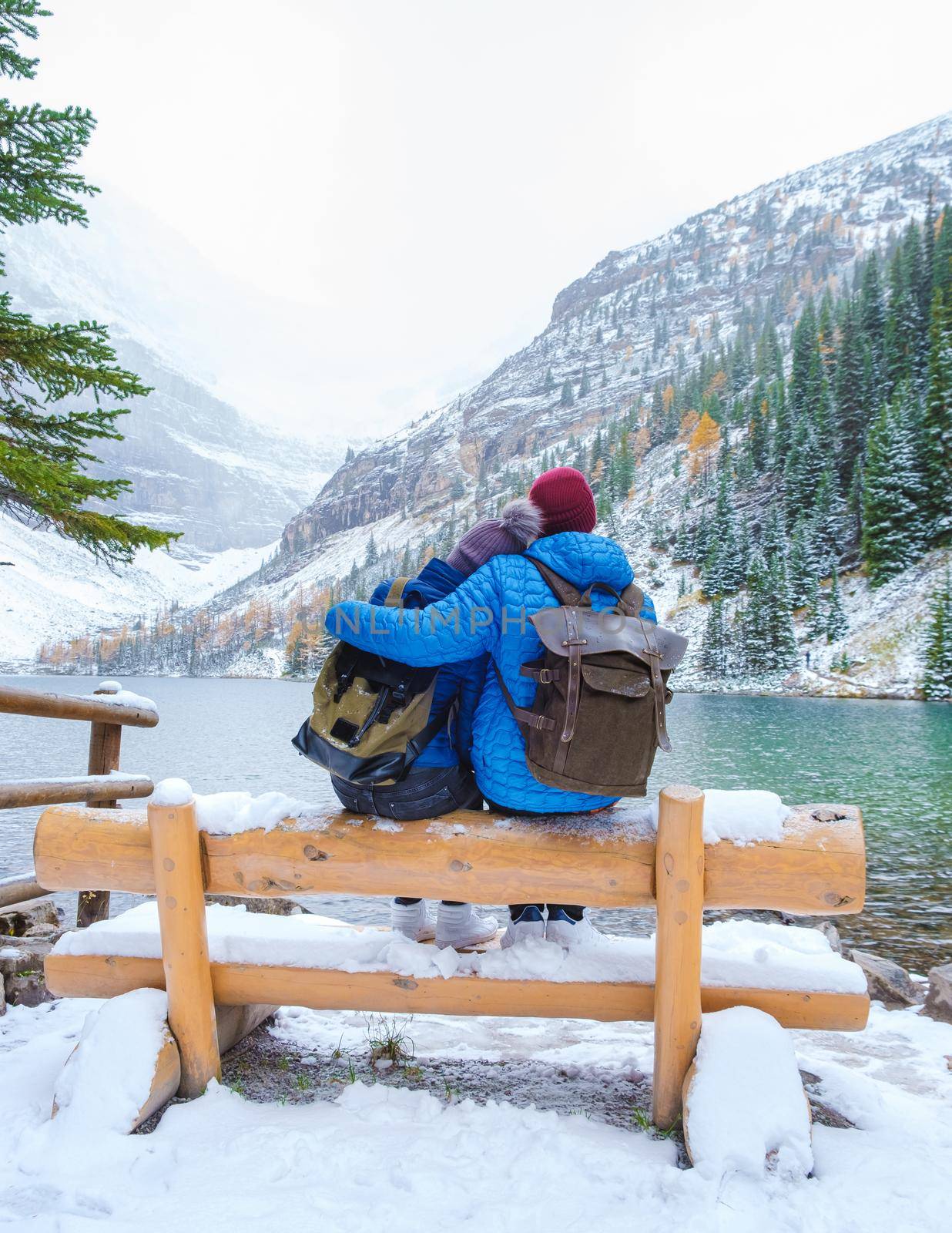 Lake Agnes by Lake Louise Banff national park is a lake in the Canadian Rocky Mountains. A young couple of men and women sitting on a bench by the lake during a cold day in Autumn in Canada with snow