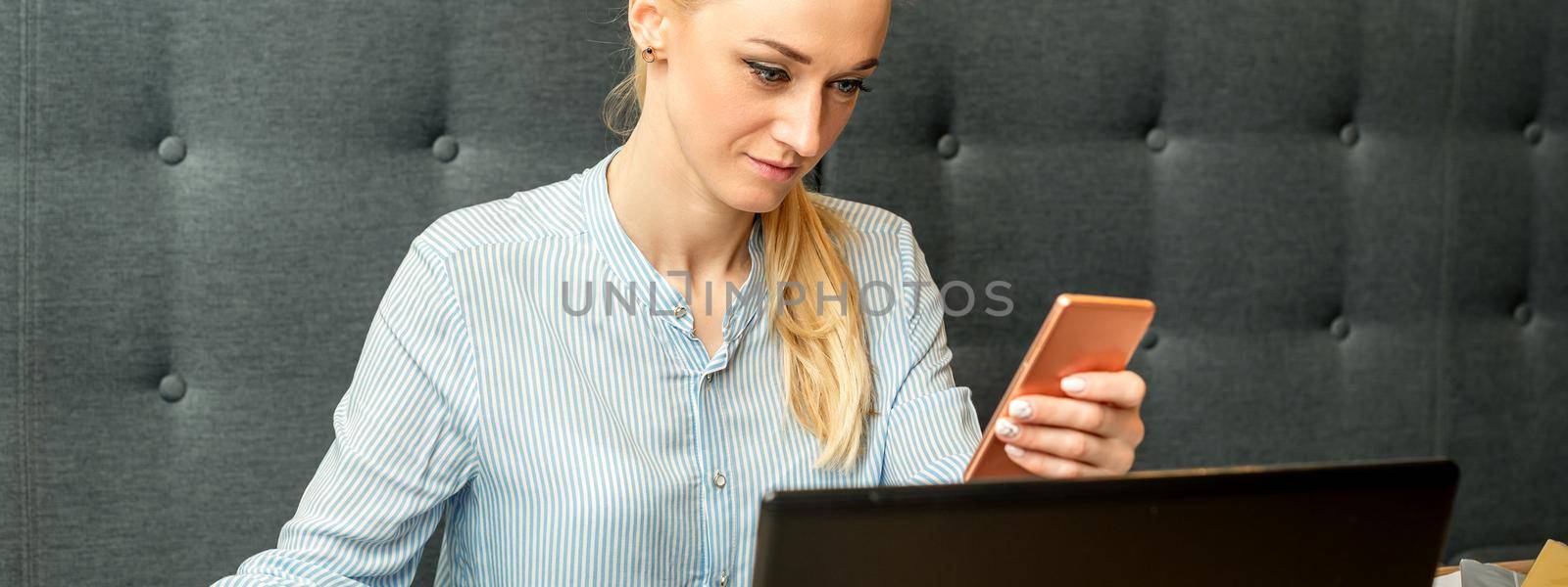 Young businesswoman using smartphone sitting at the table with laptop in cafe