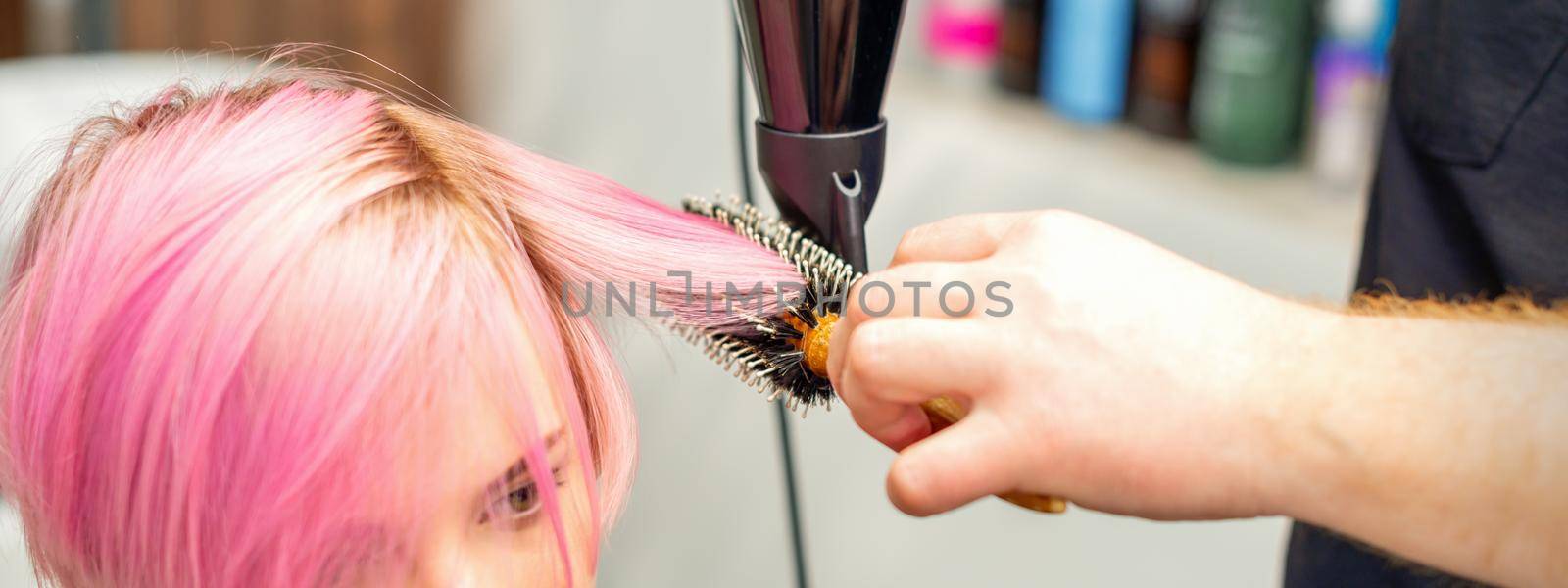 Hairdresser dries pink hair of the young woman in a beauty salon