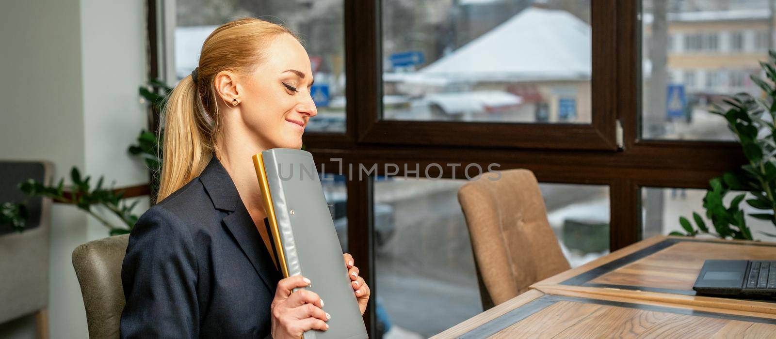 Beautiful young caucasian businesswoman holding a folder with documents sitting at the table in office or cafe