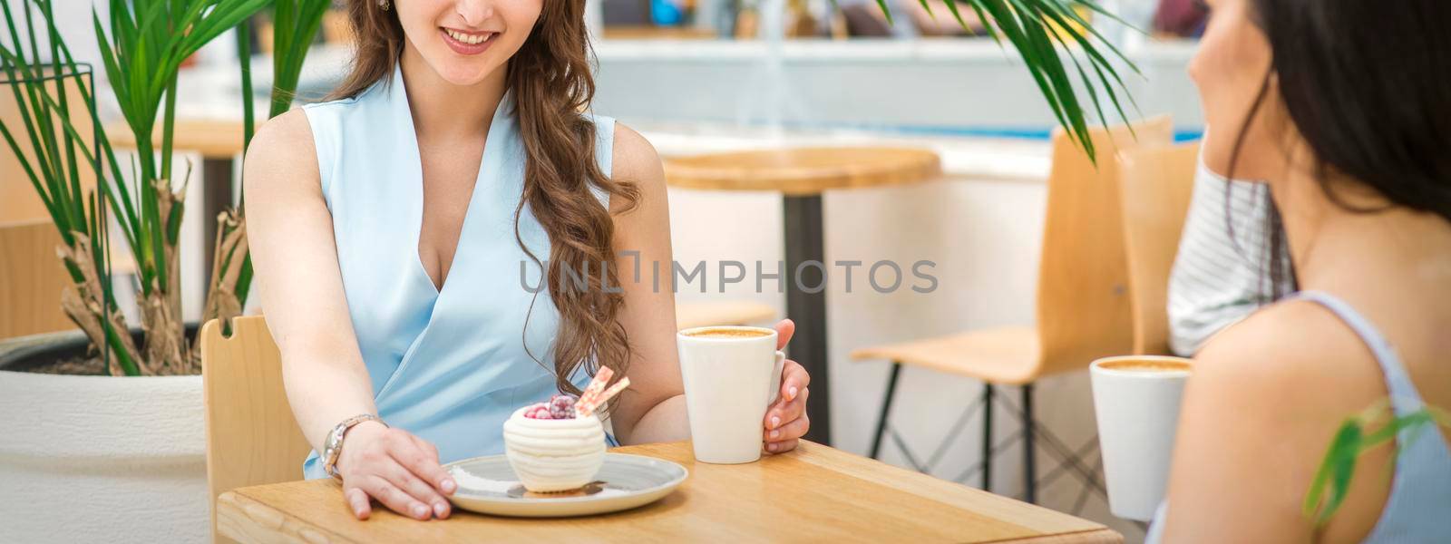 Two beautiful young caucasian women drink coffee sitting at the table in cafe outdoor