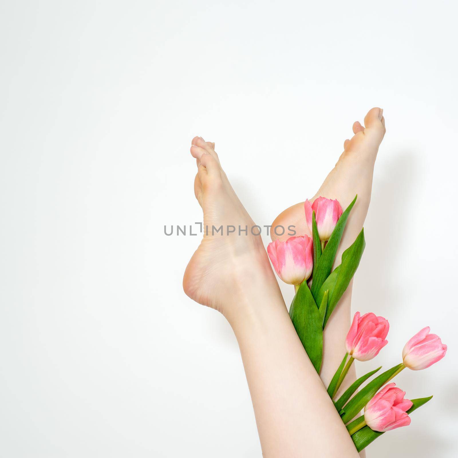 Beautiful slim smooth woman's legs with tulips flowers on white background