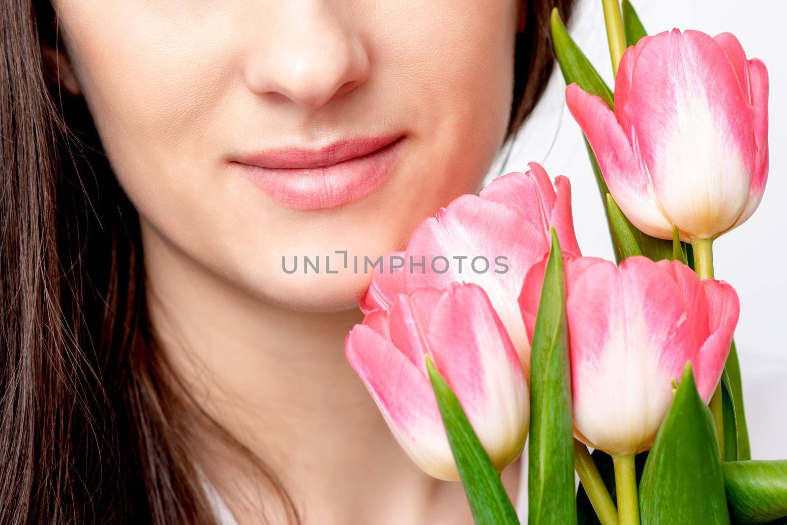 Half face portrait of a happy young caucasian woman with pink tulips against a white background