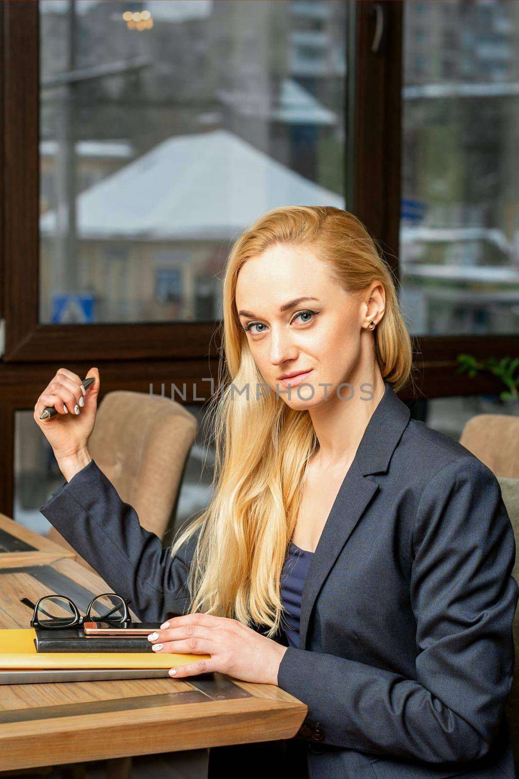 Portrait of a young caucasian businesswoman with documents and laptop at the table looking at the camera in cafe