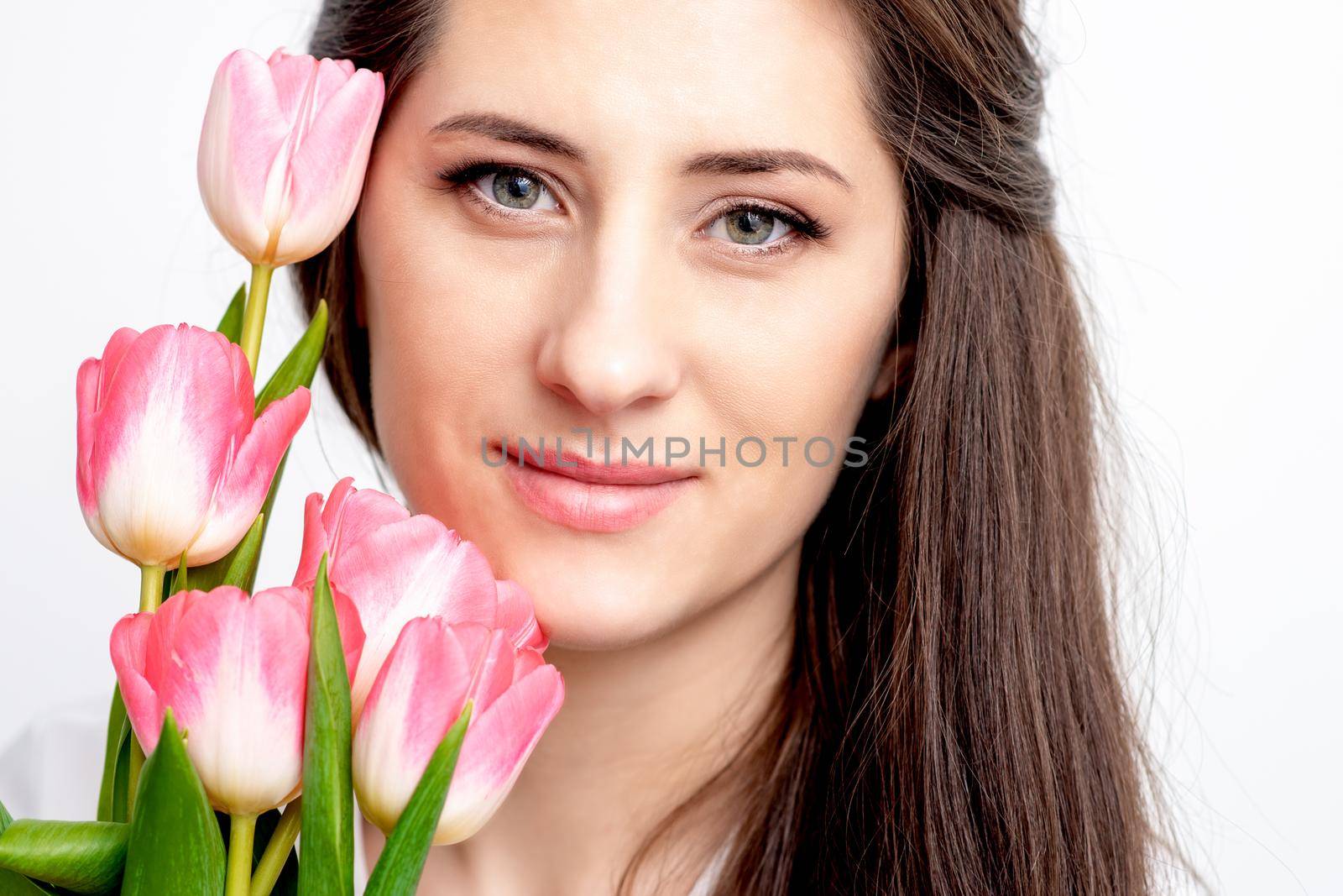 Portrait of a happy young caucasian woman with pink tulips against a white background