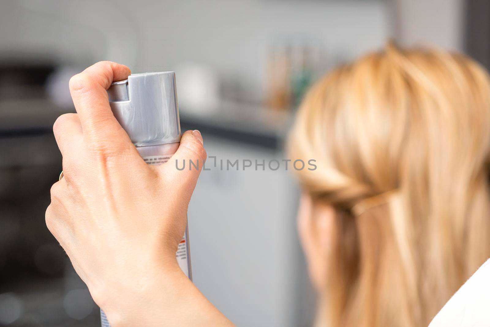 Closeup of hair spray in the hand of hairstylist while fixing blonde hair of the young woman in a beauty salon