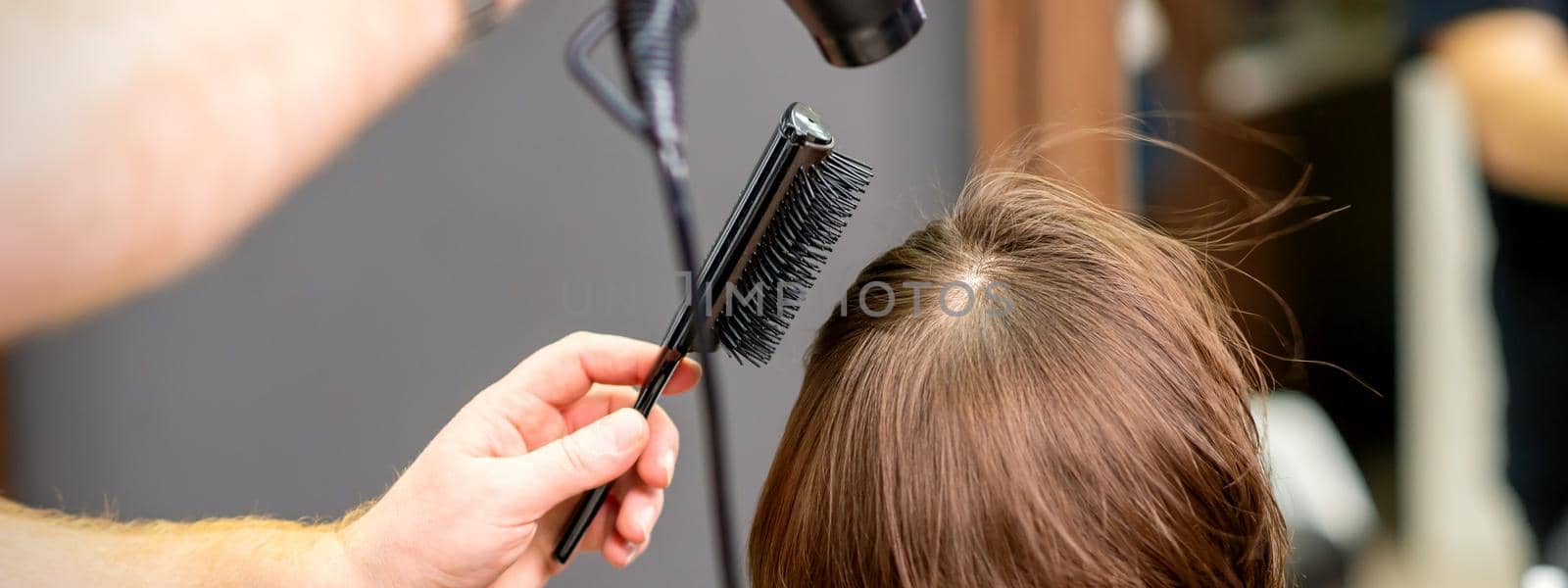 Hairdresser dries brown hair of the young woman in a beauty salon