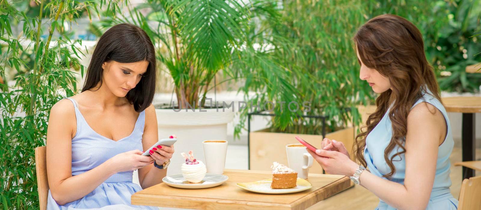 Two young women looking their smartphones while sitting in a cafe. Technology people addictions