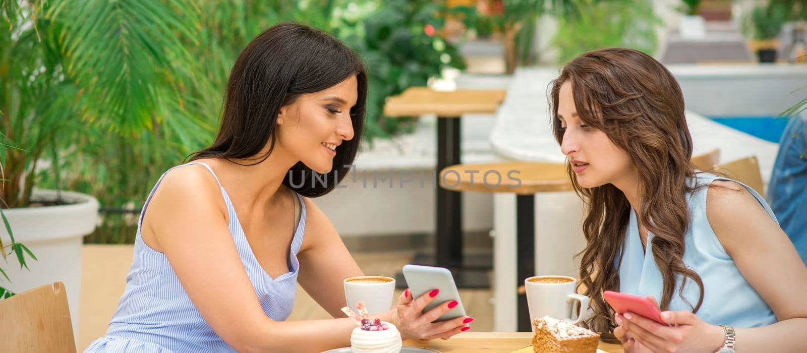 Two beautiful young women together watching something on the phone at the table in a cafe