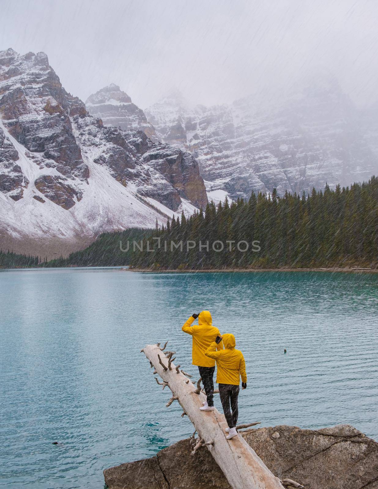 Lake moraine during a cold snowy day in Autumn in Canada, Beautiful turquoise waters of the Moraine lake with snow. couple of men and women in yellow raincoat jacket during snow